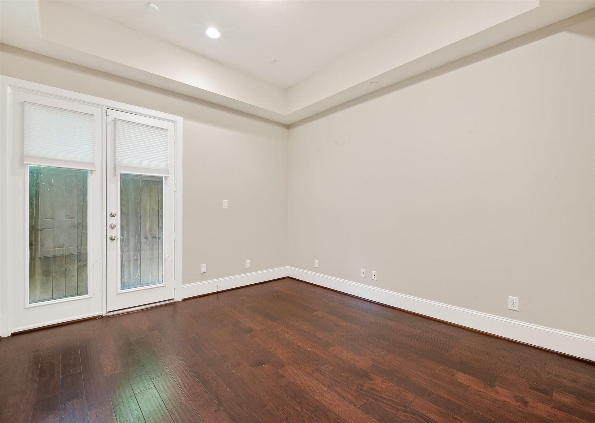 816 Yale Street, #C, Houston, TX 77007 Bright first floor bedroom with rich wood flooring, neutral paint, and recessed lighting. Features French doors with blinds leading to an outside area, creating a spacious and inviting atmosphere.