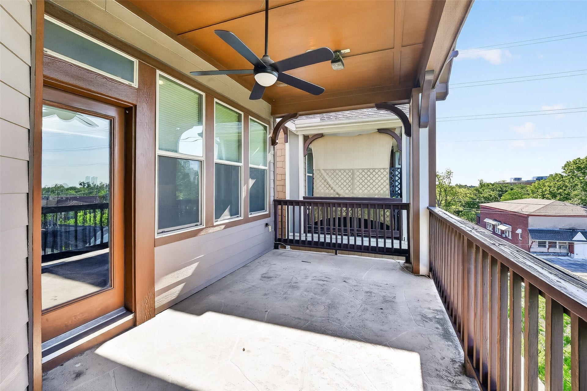 816 Yale Street, #C, Houston, TX 77007 This is a spacious covered balcony with a ceiling fan, featuring wooden railings and a view of the neighborhood. Ideal for outdoor relaxation and entertaining.
