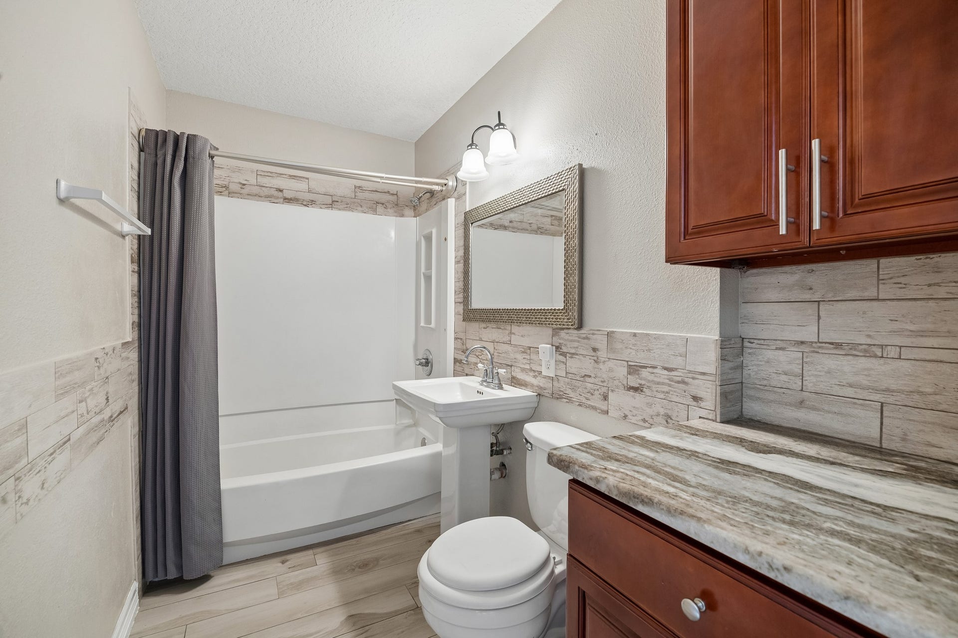 10702 Duncum Street, Houston, TX 77013 Charming bathroom featuring a sleek pedestal sink, elegant tiled walls, and rich wood cabinetry, complemented by a modern shower and tub combination.