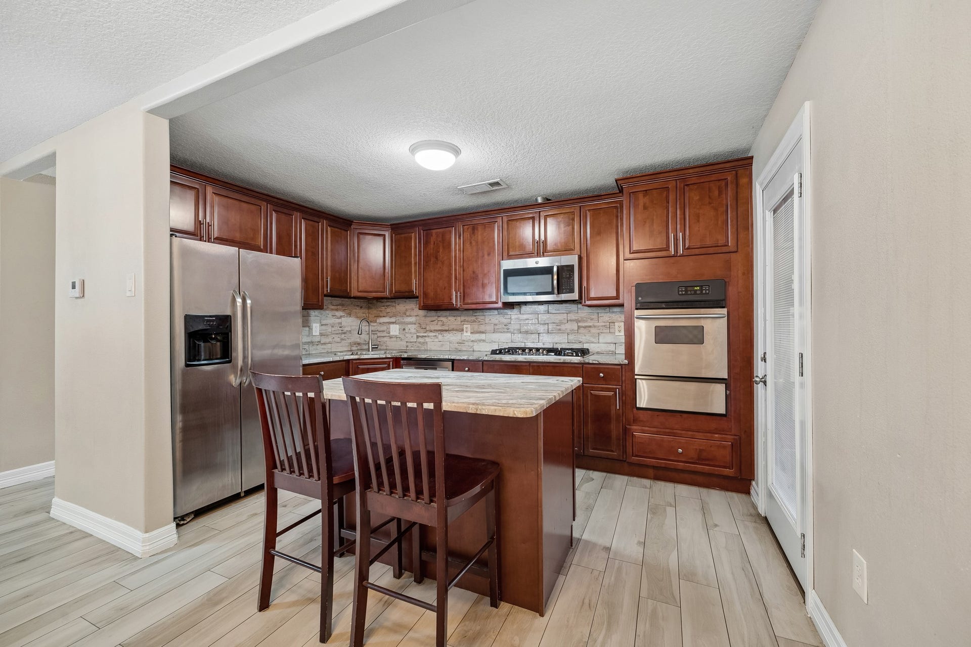 10702 Duncum Street, Houston, TX 77013 Elegant kitchen with rich wood cabinetry, a modern stainless steel refrigerator, and a built-in oven. The cozy island offers additional workspace and seating, perfect for casual dining.