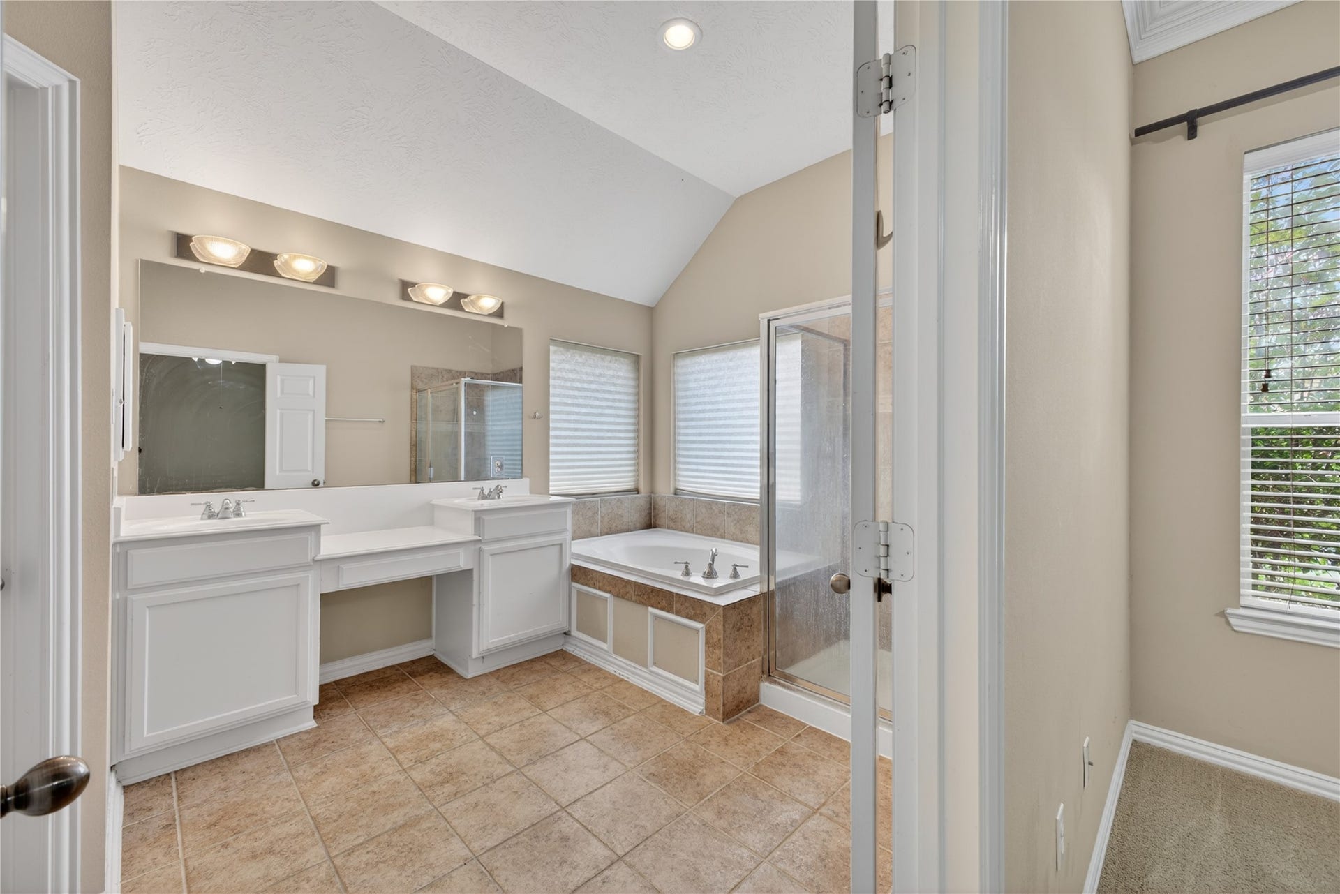 14326 Manorbier Lane, Sugar Land, TX 77498 This bathroom features a dual-sink vanity, a spacious soaking tub with tile surround, and a separate glass-enclosed shower. It has neutral tones, ample lighting, and a window for natural light.