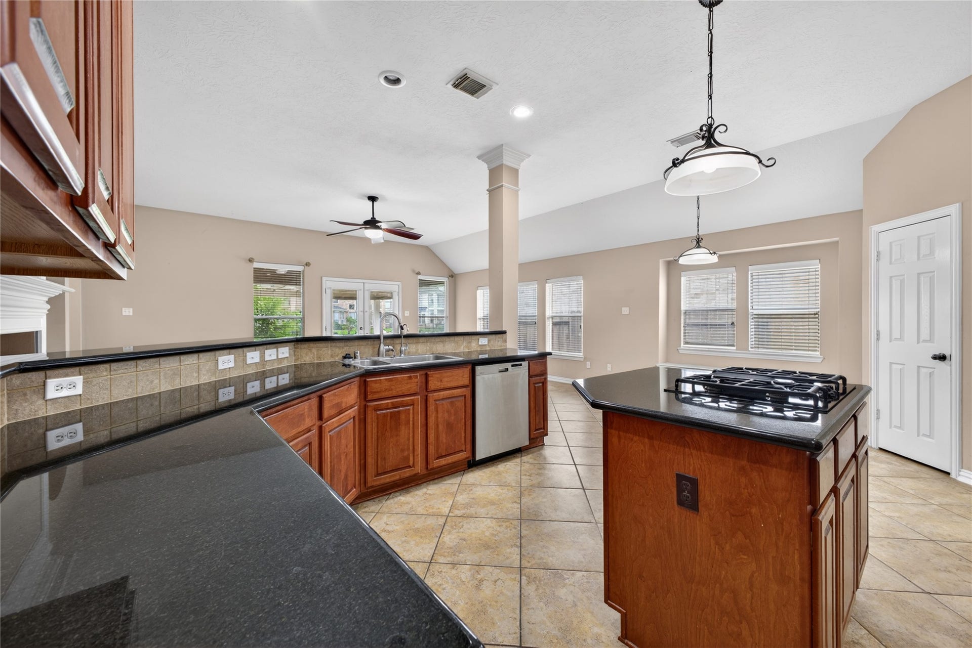 14326 Manorbier Lane, Sugar Land, TX 77498 This spacious kitchen features elegant dark countertops, rich wooden cabinets, and a central island with a cooktop. The open layout offers ample natural light, tiled floors, and modern fixtures, making it perfect for entertaining.