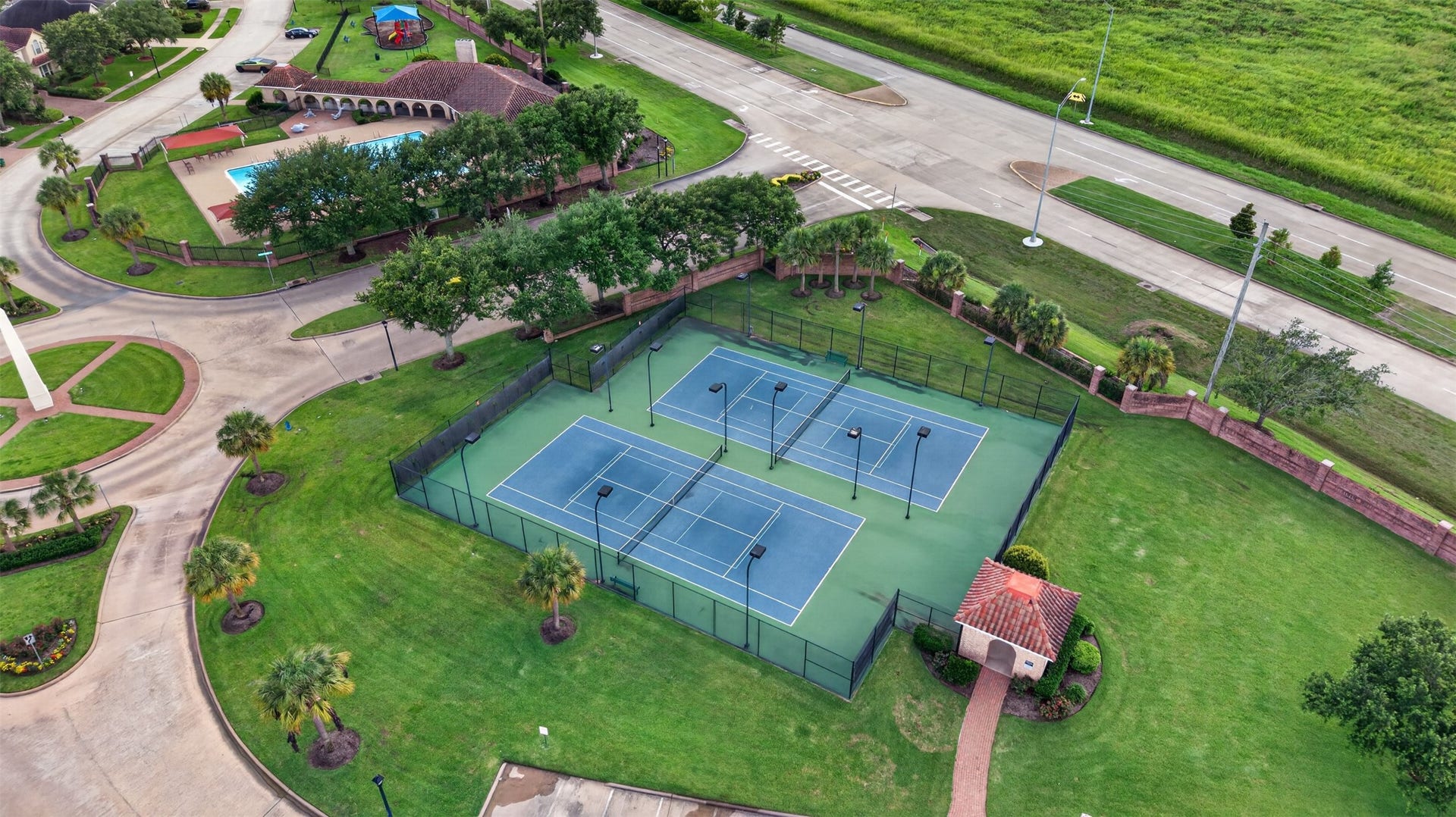 14326 Manorbier Lane, Sugar Land, TX 77498 This photo showcases a residential community with well-maintained tennis courts, a swimming pool, and a playground, surrounded by lush greenery. Ideal for active families.