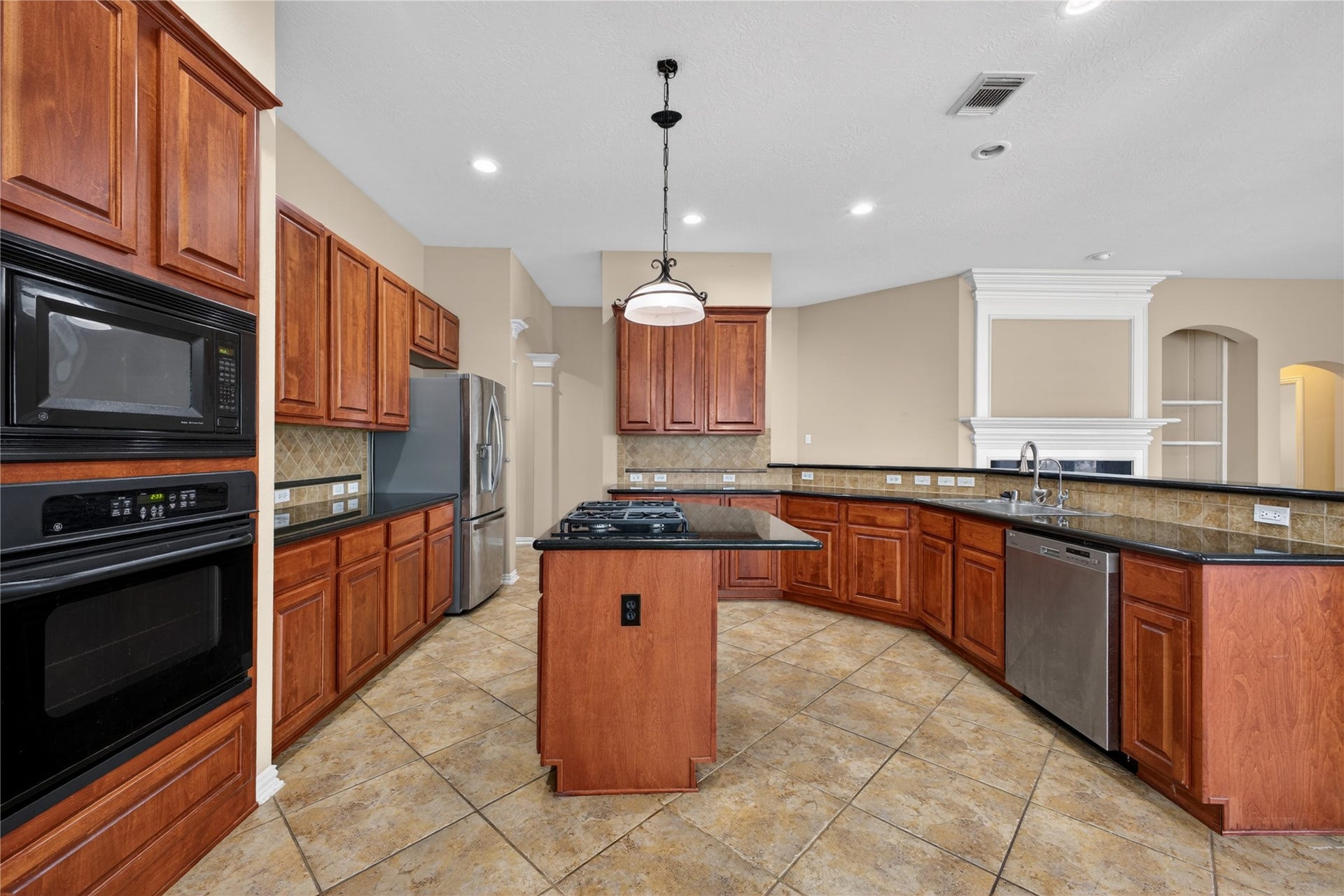 14326 Manorbier Lane, Sugar Land, TX 77498 This spacious kitchen features elegant wood cabinetry, granite countertops, a central island with a gas cooktop, and modern stainless steel appliances. The open layout flows into the living area, enhanced by tile flooring and ample lighting.