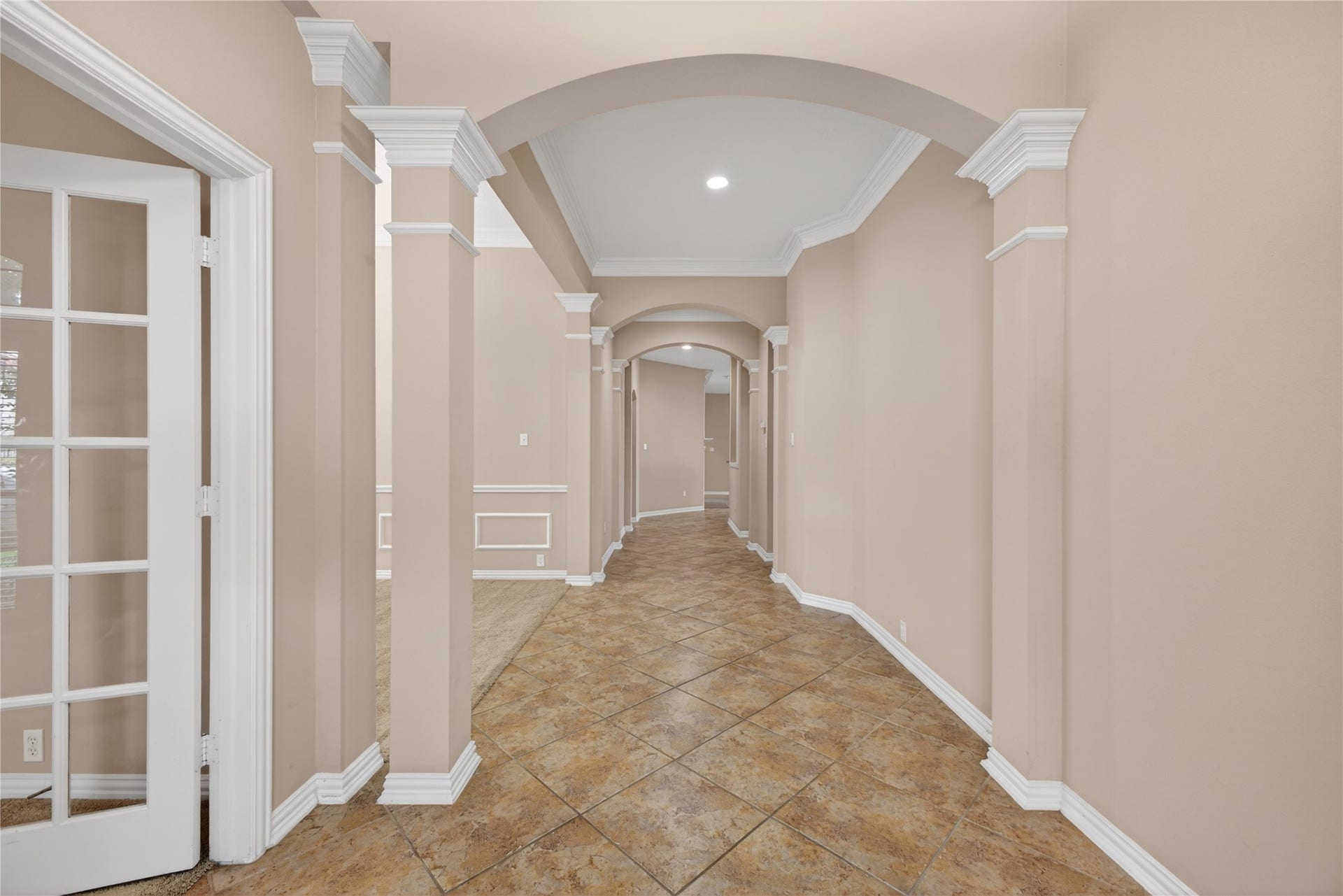 14326 Manorbier Lane, Sugar Land, TX 77498 This photo showcases an elegant hallway with arched ceilings, neutral wall tones, and tiled flooring, leading to multiple rooms. French doors on the left add a touch of sophistication.