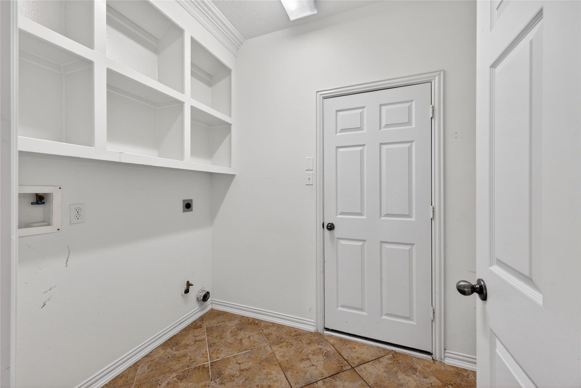 14326 Manorbier Lane, Sugar Land, TX 77498 This photo shows a utility room with white walls and built-in shelving for storage. There's a door leading out, and the space is equipped for laundry appliances. The floor features a tile finish.