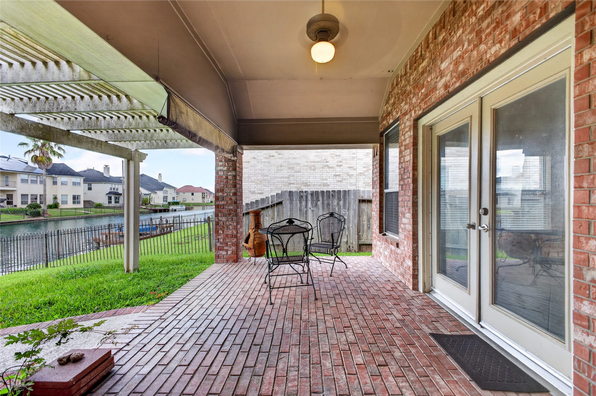 14326 Manorbier Lane, Sugar Land, TX 77498 This photo showcases a covered brick patio with ceiling fan, overlooking a serene waterfront view. The space features elegant patio furniture, a pergola for shade, and French doors leading indoors, perfect for outdoor relaxation and entertaining.