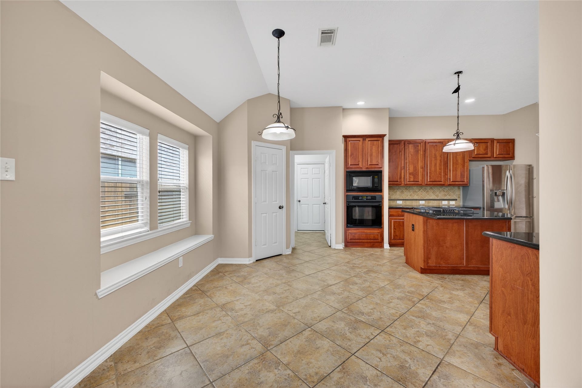 14326 Manorbier Lane, Sugar Land, TX 77498 Bright kitchen with tiled floors, granite countertops, and wooden cabinetry. Features a breakfast nook with a bench seat by the windows, stainless steel appliances, and pendant lighting.