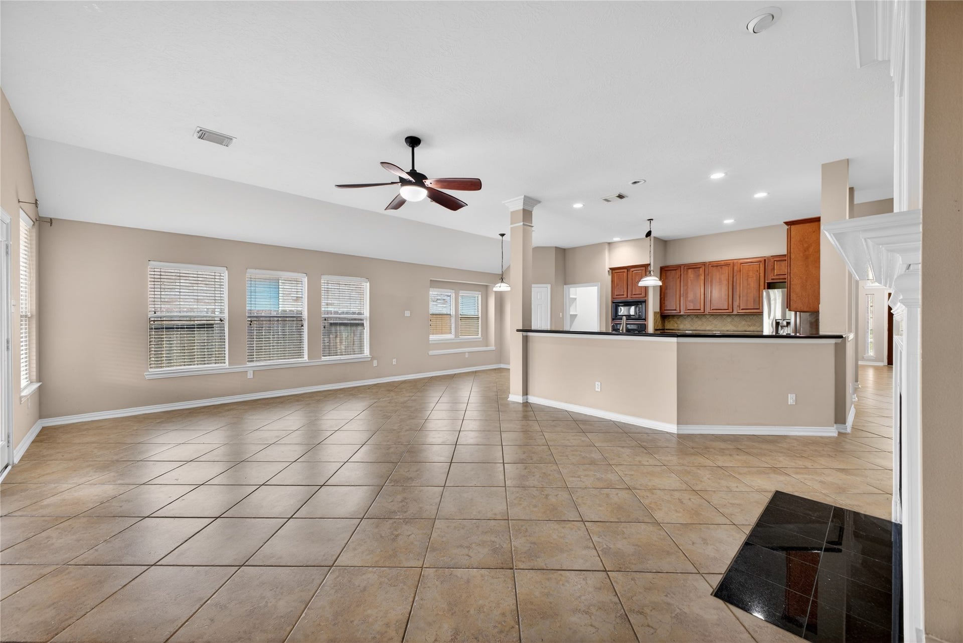 14326 Manorbier Lane, Sugar Land, TX 77498 This spacious, open-concept living area features large tile flooring, neutral walls, and ample natural light through multiple windows. The modern kitchen includes wooden cabinetry, a central island, and stainless steel appliances, seamlessly connecting to the living space. A ceiling fan and recessed lighting add to the room's functionality and comfort.