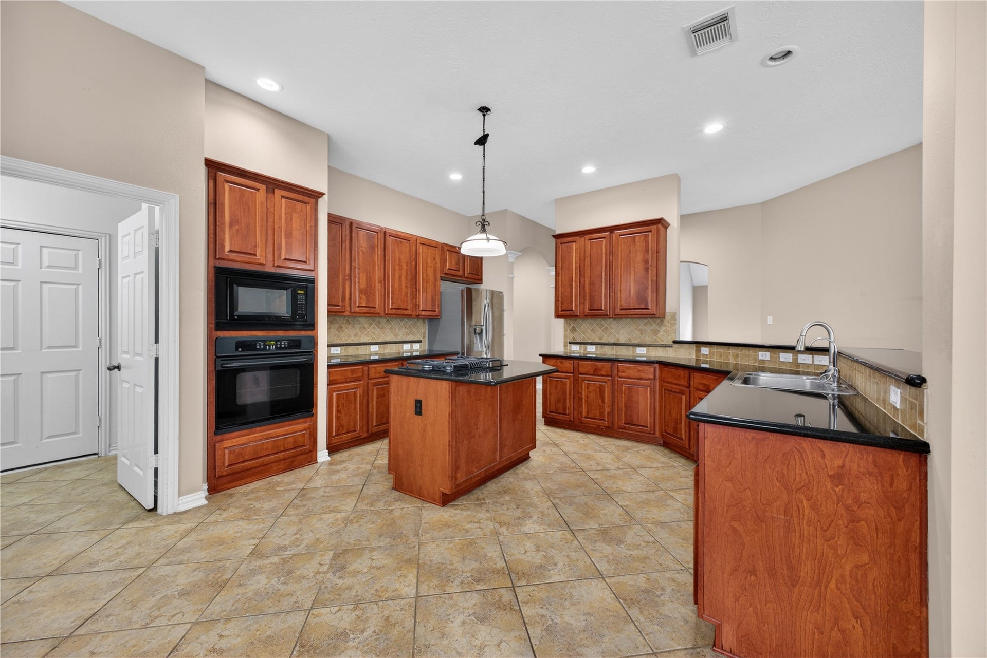 14326 Manorbier Lane, Sugar Land, TX 77498 This spacious kitchen features rich wood cabinetry, granite countertops, and a central island. It includes built-in appliances, abundant storage, and tiled flooring, creating a warm and functional cooking space.