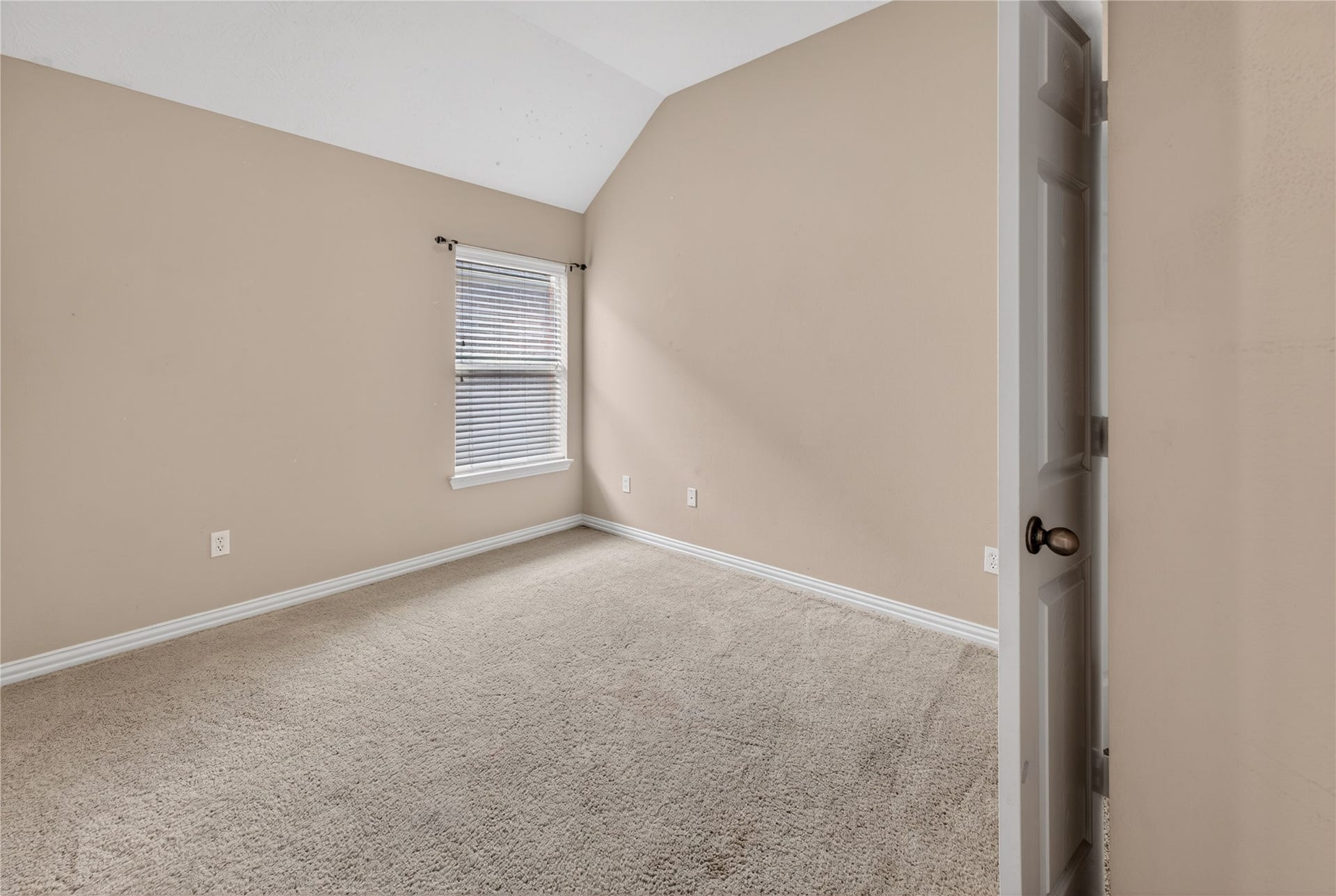 14326 Manorbier Lane, Sugar Land, TX 77498 This photo shows a cozy, carpeted room with soft beige walls and a single window bringing in natural light. The room features a sloped ceiling and a small door, creating a simple and inviting space.