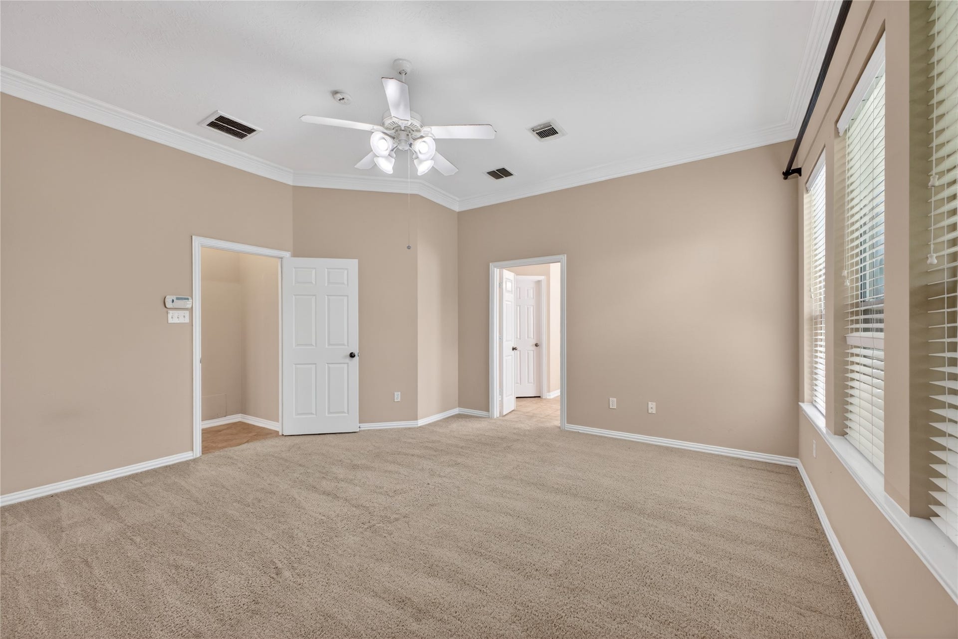 14326 Manorbier Lane, Sugar Land, TX 77498 This room features neutral-toned walls and carpeting, with ample natural light from large windows. It includes a ceiling fan, crown molding, and access to adjacent rooms through white doors, offering a bright and spacious feel.