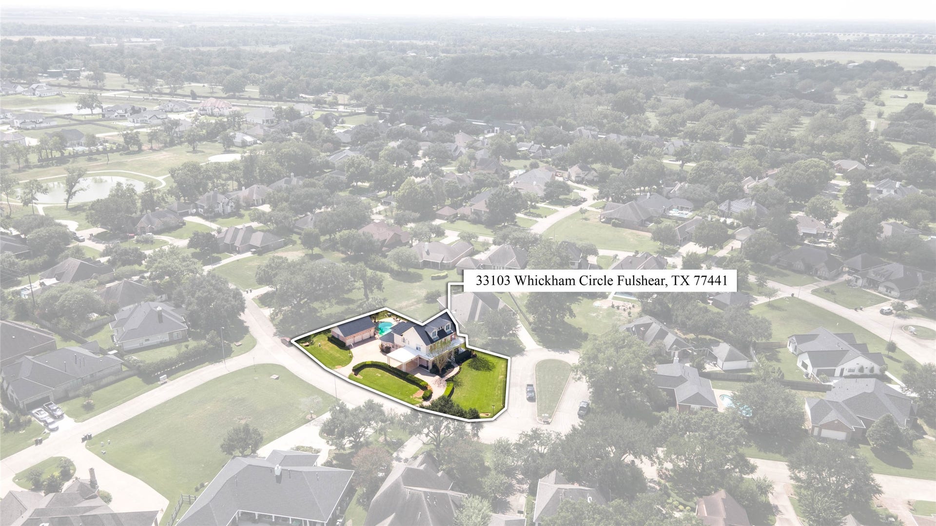 33103 Whickham Circle, Fulshear, TX 77441 This elevated aerial showcases the residence within its surrounding neighborhood, highlighting the homes prominent position, expansive lawn, detached garage, & private pool & spa.