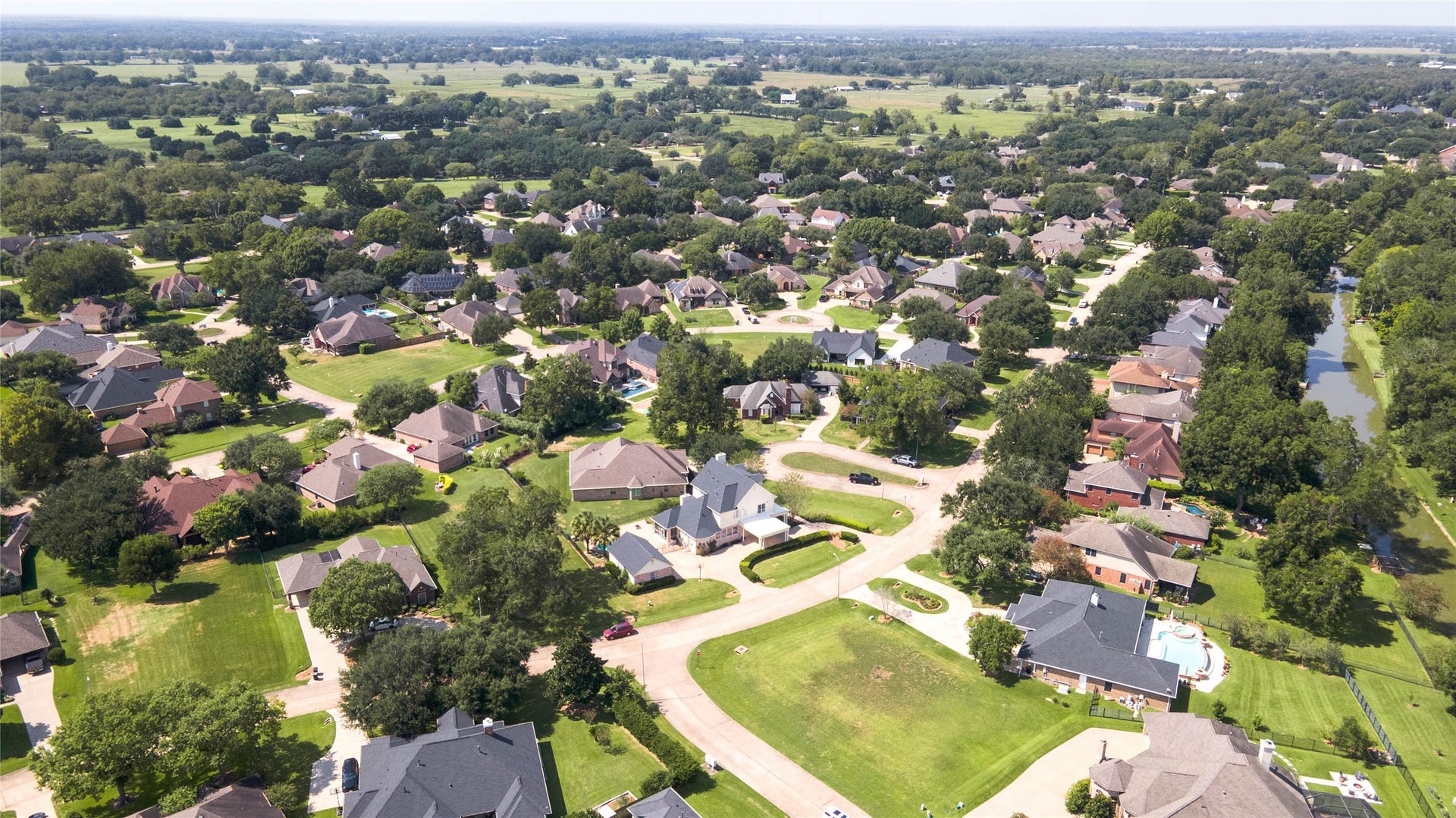 33103 Whickham Circle, Fulshear, TX 77441 A sweeping aerial view captures the surrounding residential landscape, characterized by winding streets, mature tree canopies, spacious homesites, and extensive green space.