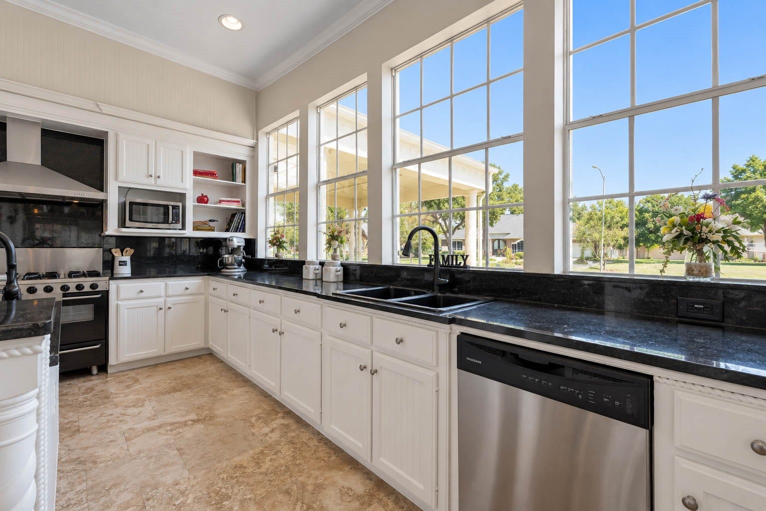 33103 Whickham Circle, Fulshear, TX 77441 This remarkable wall of windows spans the kitchen, bathing the space in natural light and offering beautiful outdoor views. Below, an extended run of dark granite counters and white cabinetry provides abundant storage and workspace, complemented by dual sinks and a stainless dishwasher.