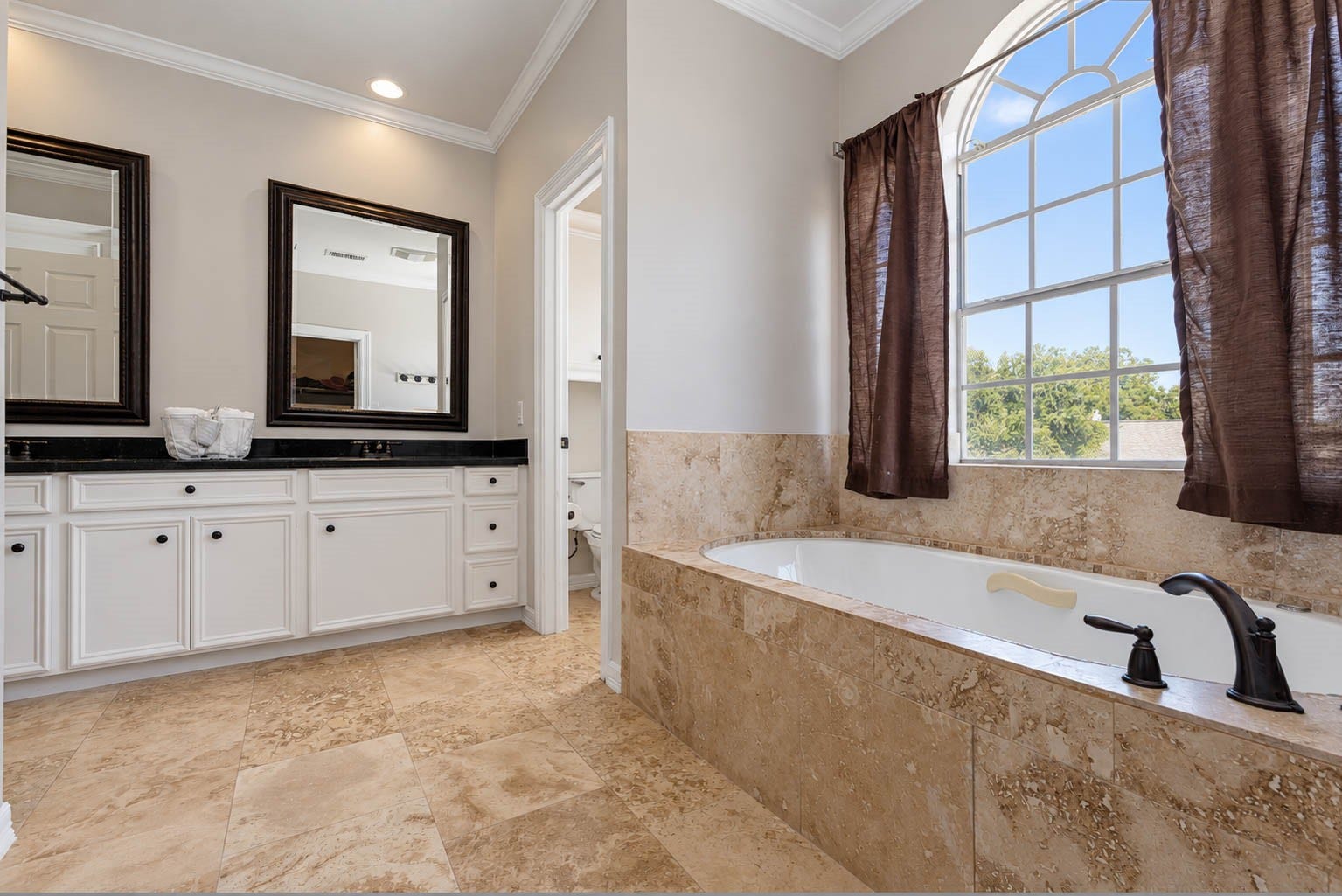 33103 Whickham Circle, Fulshear, TX 77441 A large jetted tub with an elegant tile surround rests beneath an oversized arched window, where abundant natural light enhances the baths serene, spa-inspired ambiance.
