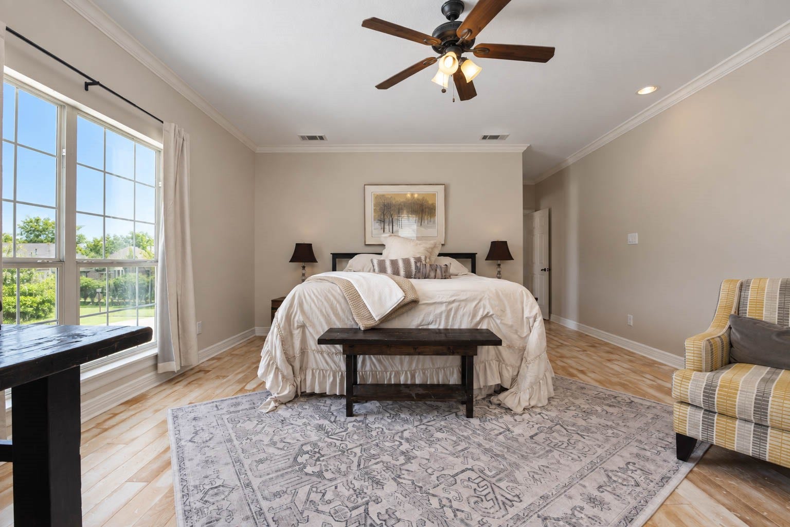 33103 Whickham Circle, Fulshear, TX 77441 An alternate perspective emphasizes the impressive scale of the primary retreat, where large windows introduce abundant natural light and frame exterior views. Hardwood flooring and a neutral palette lend an understated elegance to the relaxing space.