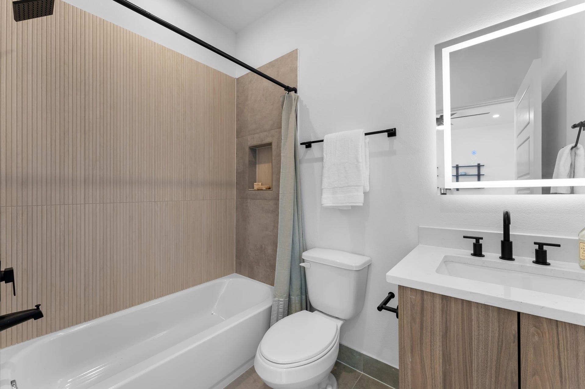 This first-floor full bathroom, located within a secondary bedroom, features a sleek vanity with a quartz countertop and a convenient shower/tub combo, blending modern finishes with everyday functionality for comfort and style.