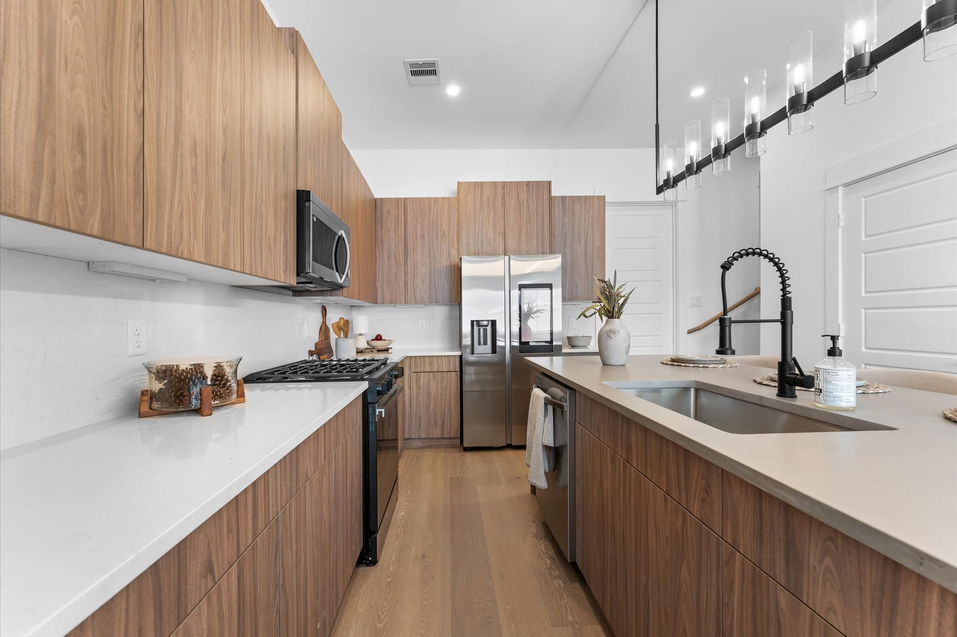 The kitchen, the heart of the second-floor open-concept living, dining, and kitchen, features a spacious island with a one-sided cascade quartz countertop, farmhouse sink, and modern pendant lights, complemented by an abundance of sleek, modern cabinetry providing ample storage, perfect for meal prep, casual breakfasts, or gathering with family and friends.