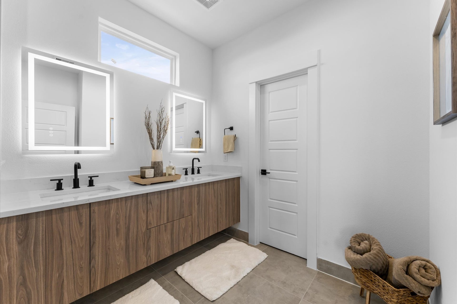 The luxurious primary ensuite features sleek modern finishes, a glass-enclosed shower with stylish tile, and a double-sink vanity topped with quartz countertops, complemented by two contemporary mirrors and lighting fixtures, creating a bright, elegant, and functional retreat.