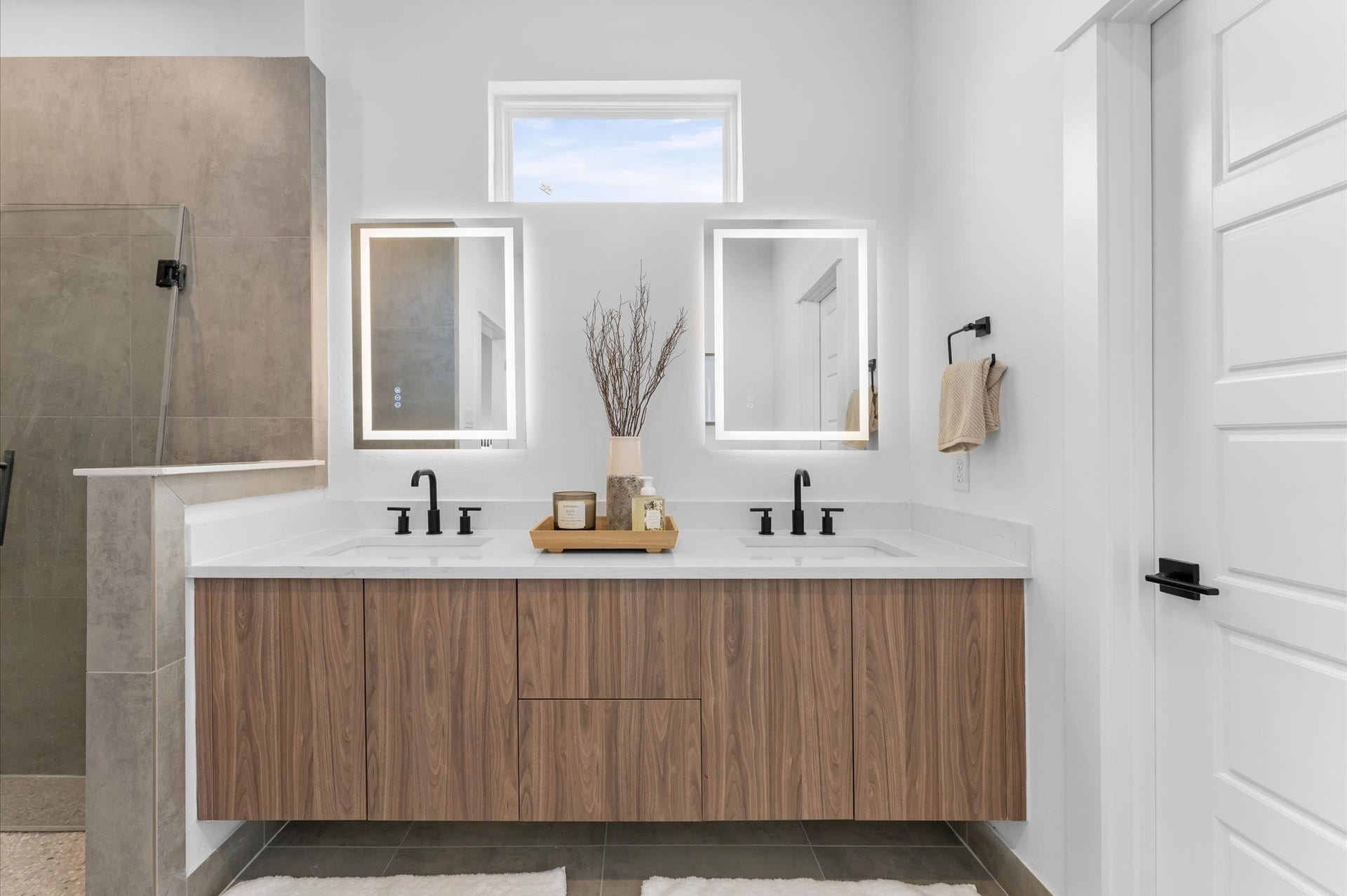 The luxurious primary ensuite features sleek modern finishes, a glass-enclosed shower with stylish tile, and a double-sink vanity topped with quartz countertops, complemented by two contemporary mirrors and lighting fixtures, creating a bright, elegant, and functional retreat.