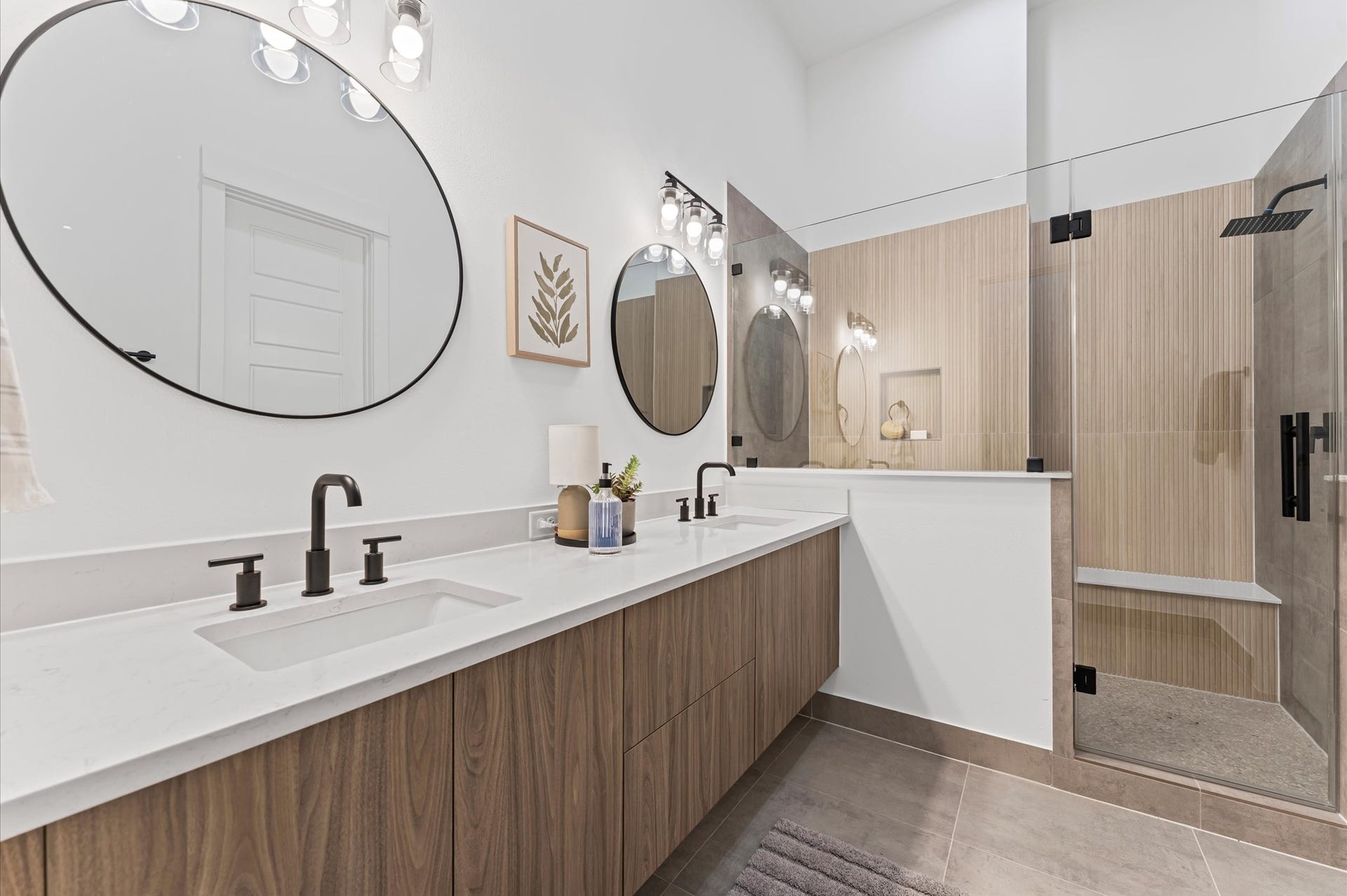 The luxurious primary ensuite features sleek modern finishes, a glass-enclosed shower with stylish tile, and a double-sink vanity topped with quartz countertops, complemented by two contemporary mirrors and lighting fixtures, creating a bright, elegant, and functional retreat.