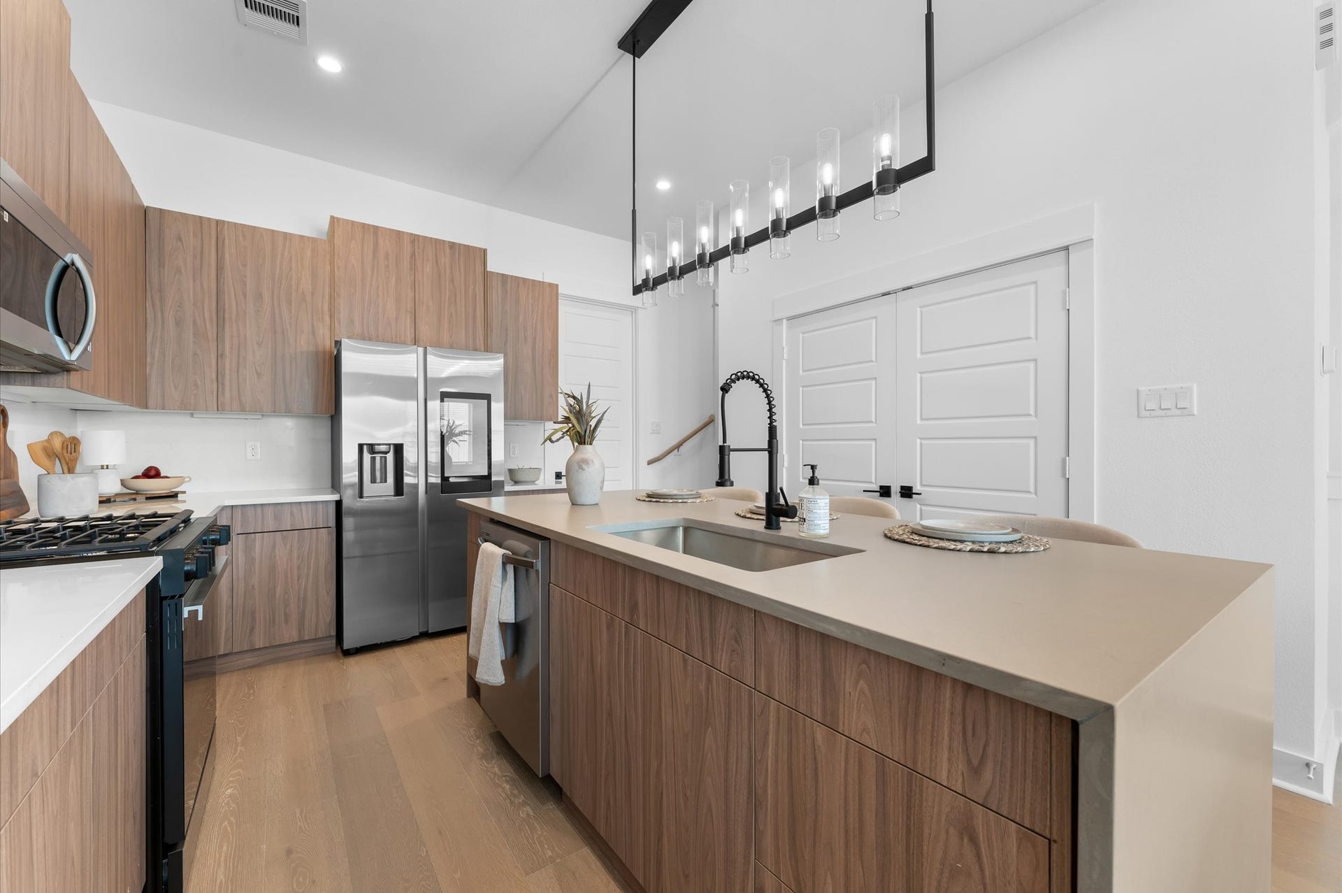 The kitchen, the heart of the second-floor open-concept living, dining, and kitchen, features a spacious island with a one-sided cascade quartz countertop, farmhouse sink, and modern pendant lights, complemented by an abundance of sleek, modern cabinetry providing ample storage, perfect for meal prep, casual breakfasts, or gathering with family and friends.