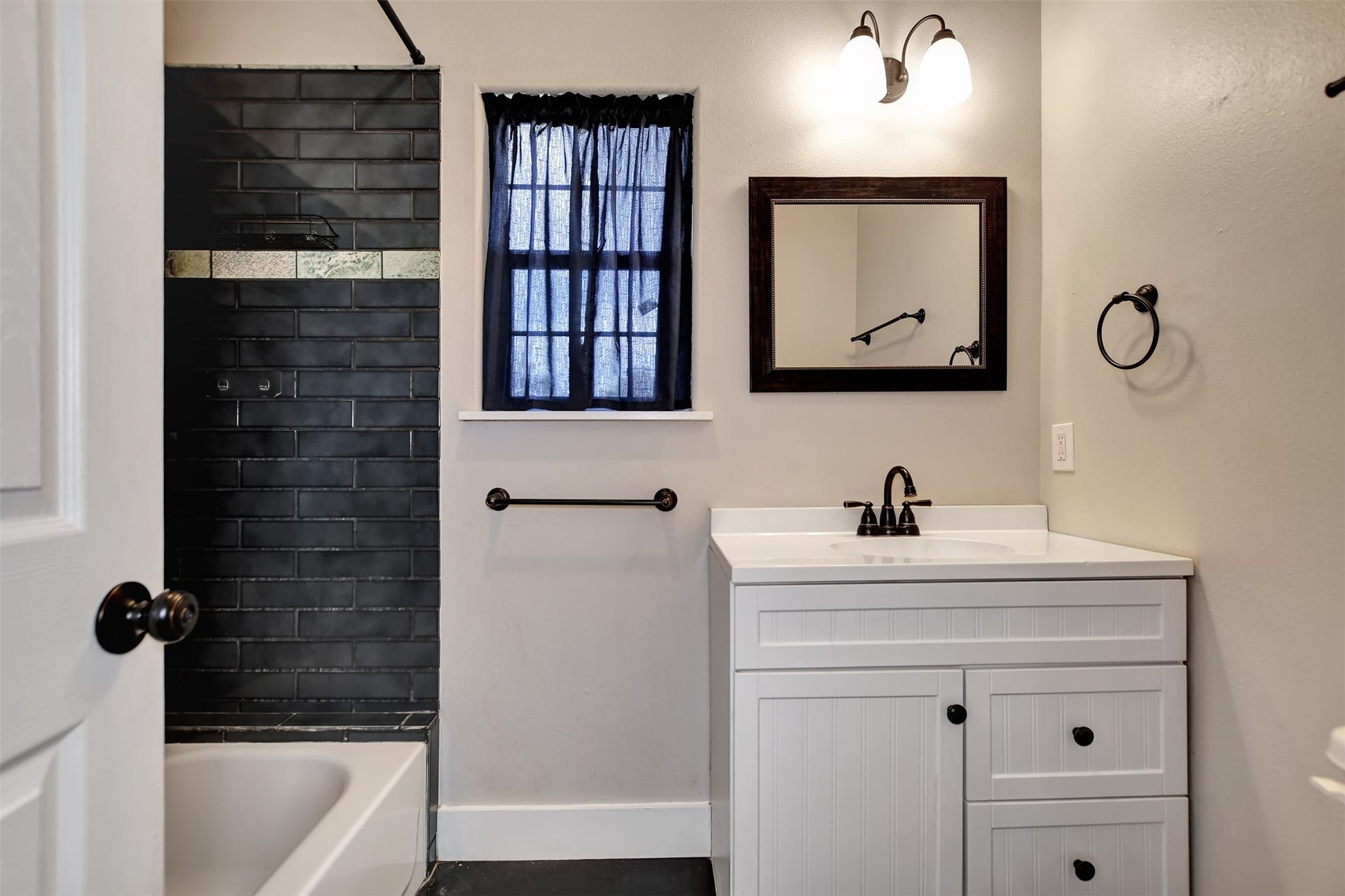 2546 16th Street, Hempstead, TX 77445 This is a well-lit primary bathroom with a black-tiled shower area, a white vanity cabinet with a sink & a framed mirror.