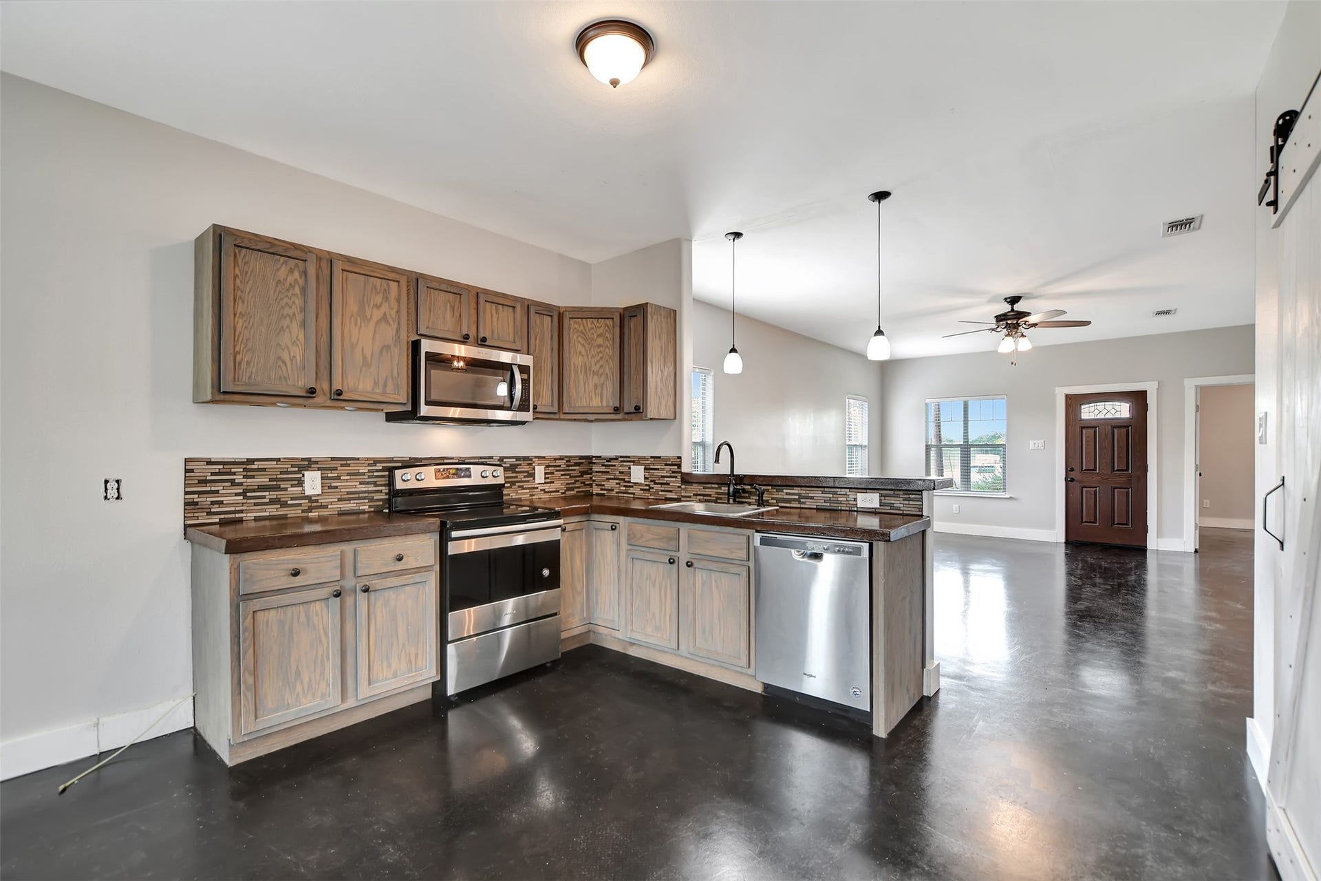 2546 16th Street, Hempstead, TX 77445 Modern kitchen with stainless steel appliances and ample cabinet space. Open floor plan with polished concrete floors, leading to a well-lit living area with ceiling fan.
