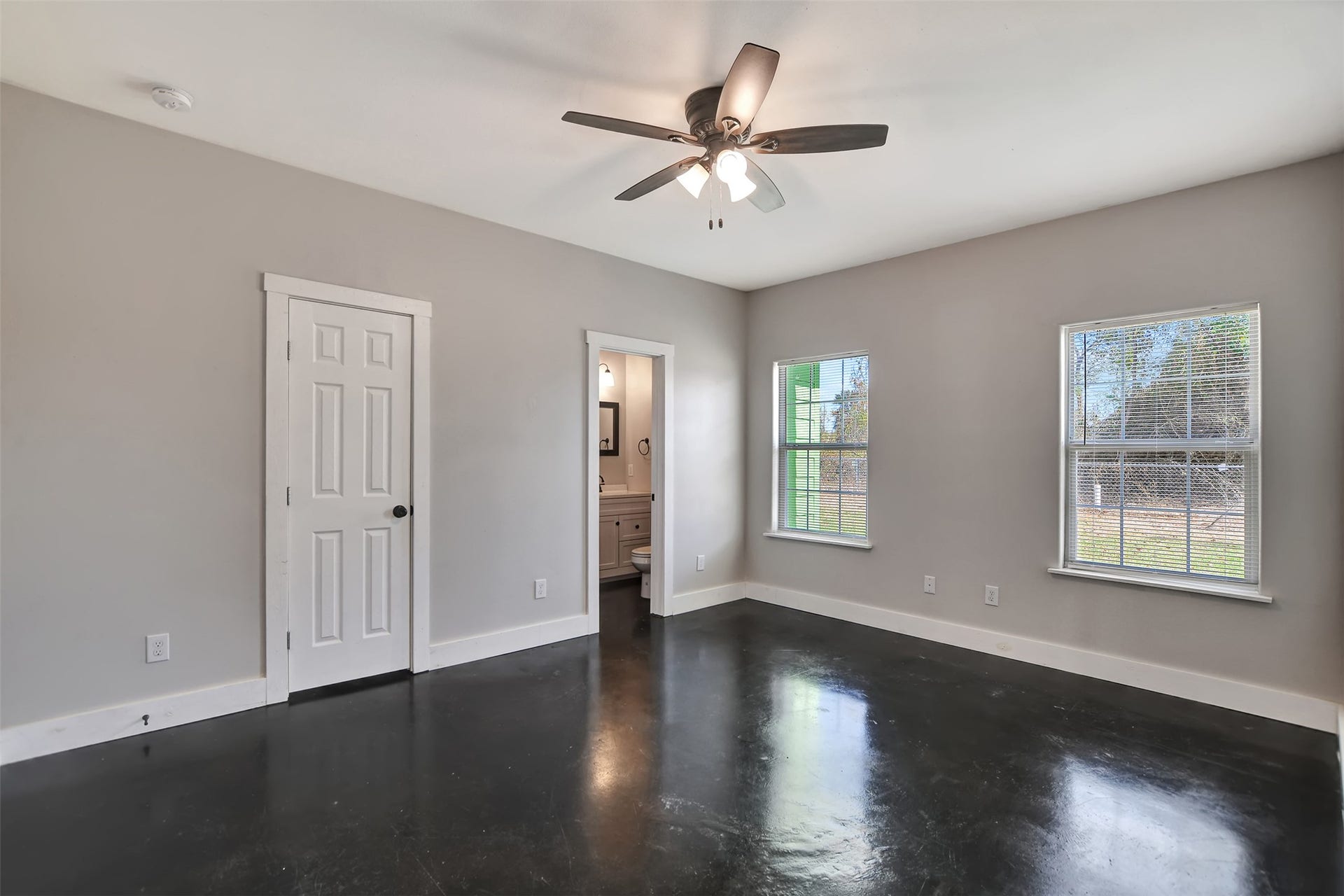 2546 16th Street, Hempstead, TX 77445 This is a spacious primary room with a modern ceiling fan, glossy dark floors, neutral wall color, and two large windows allowing natural light.