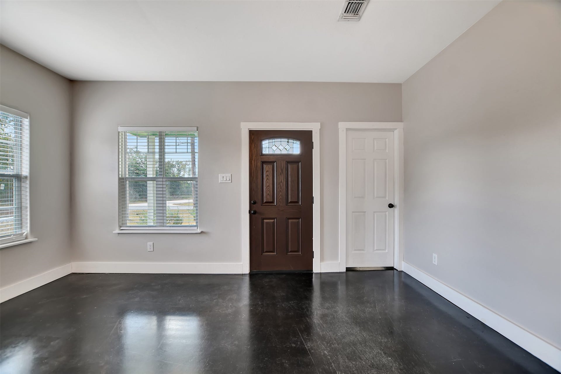 2546 16th Street, Hempstead, TX 77445 This is a bright, empty room with neutral walls, polished concrete floors, windows providing natural light, and a front door with a decorative glass insert.