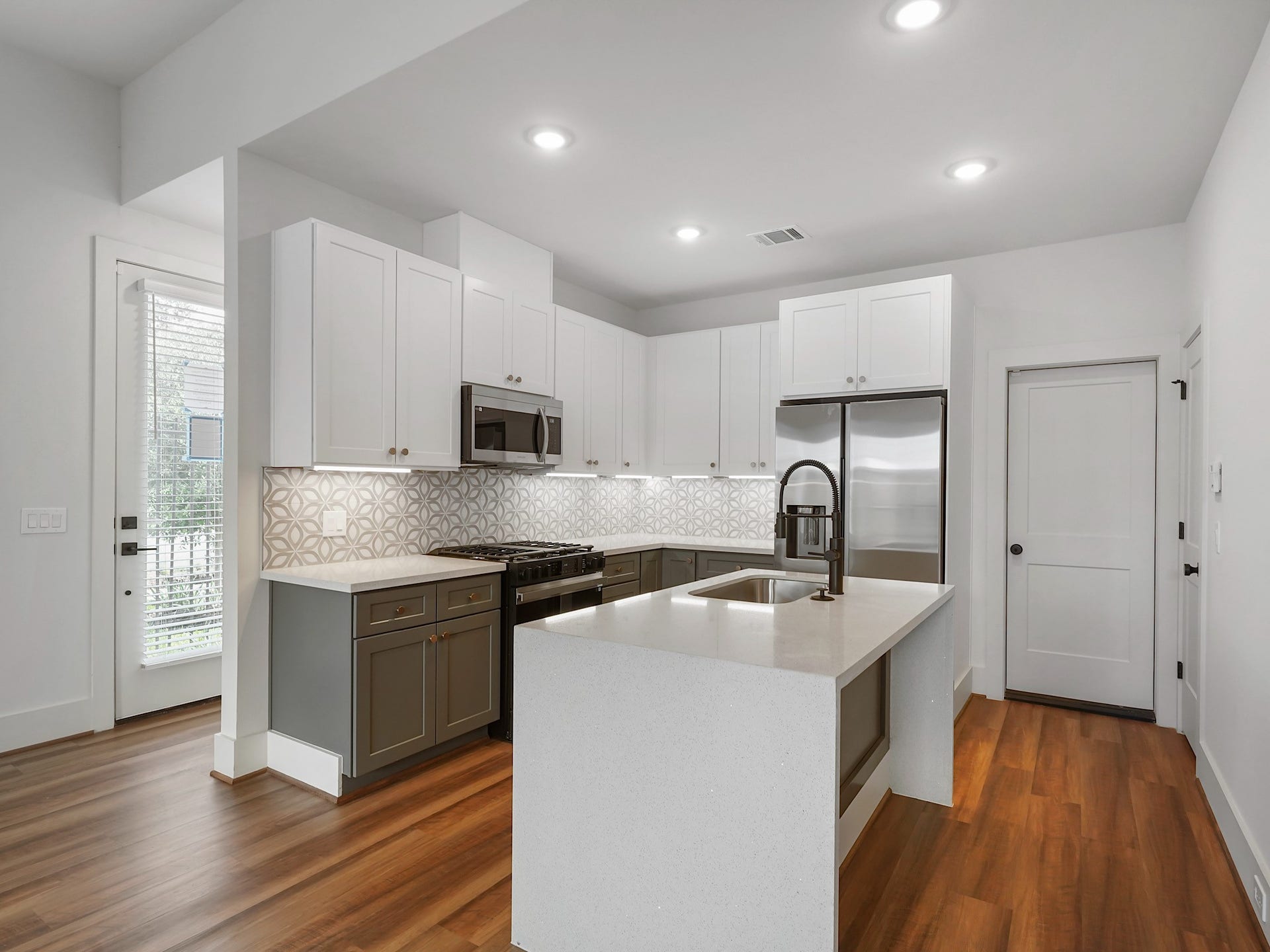 881 Rachel Street, #A, Houston, TX 77091 Modern kitchen with sleek white cabinetry, stainless steel appliances, and a stylish geometric backsplash. It features a central island with a sink, wood flooring, and ample lighting.
Photo Disclaimer: Photos are representative of the community and may depict a similar floor plan, model home, or previously completed residence.