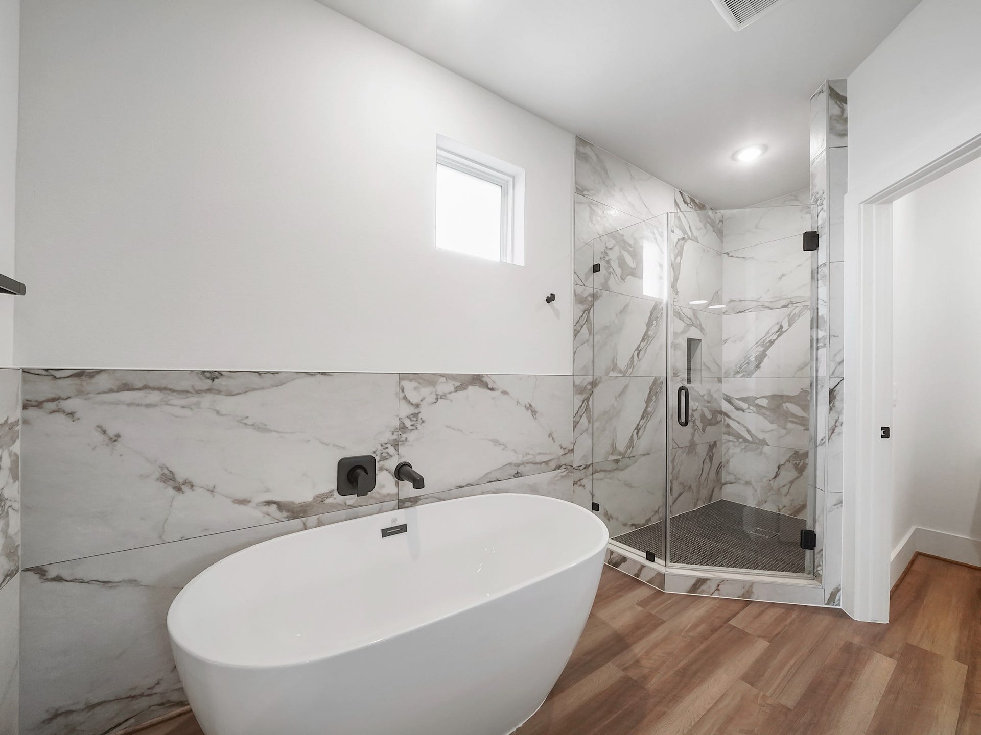 881 Rachel Street, #A, Houston, TX 77091 This modern bathroom features a sleek freestanding bathtub and a spacious glass-enclosed shower. The room is accented with elegant marble tile and warm wood flooring, creating a luxurious and inviting atmosphere.
Photo Disclaimer: Photos are representative of the community and may depict a similar floor plan, model home, or previously completed residence.