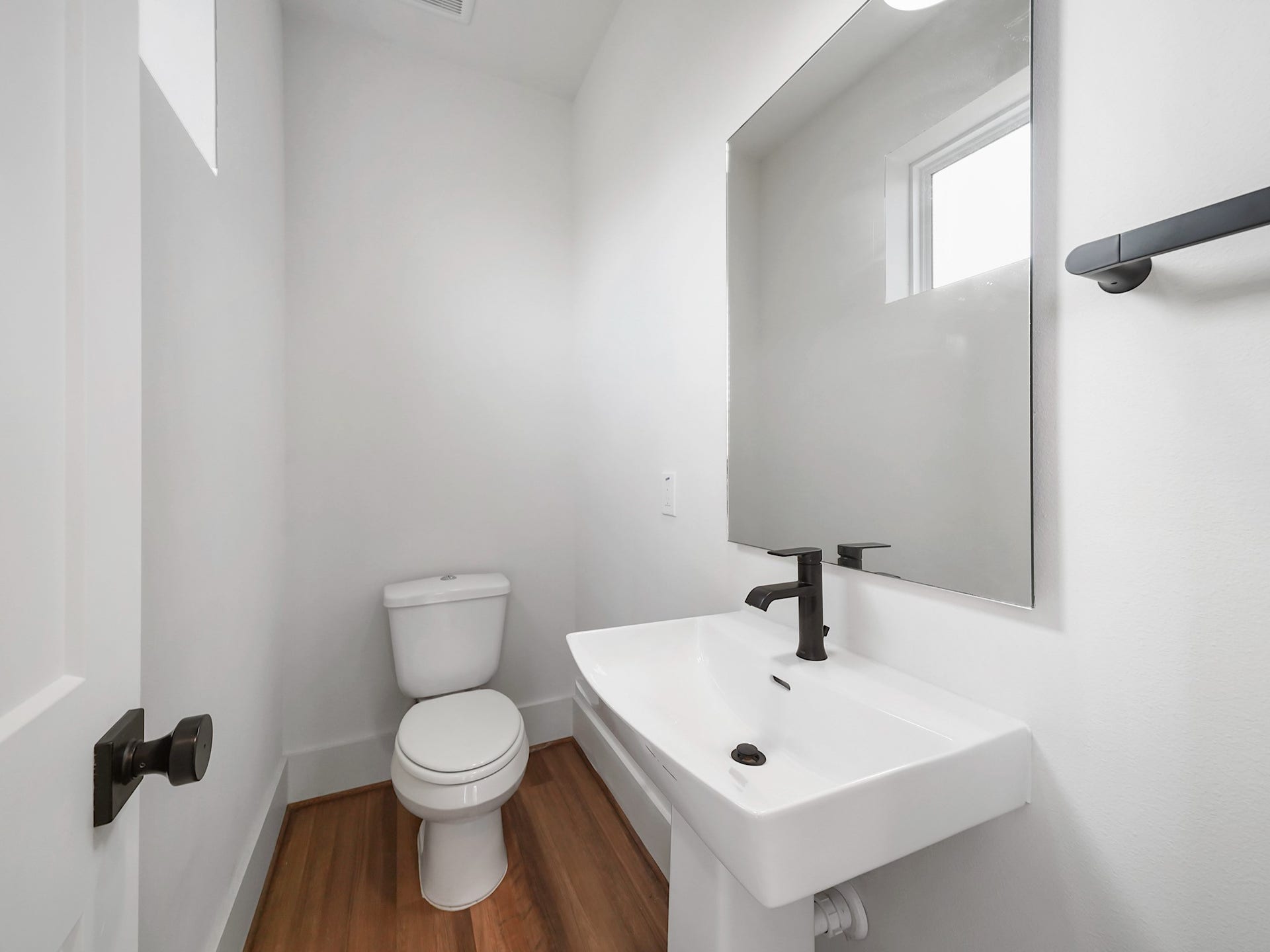 881 Rachel Street, #A, Houston, TX 77091 This is a modern, minimalist bathroom with a white toilet and sink, featuring a sleek black faucet. It has a large mirror, bright white walls, and wood flooring, creating a clean and airy feel.
Photo Disclaimer: Photos are representative of the community and may depict a similar floor plan, model home, or previously completed residence.