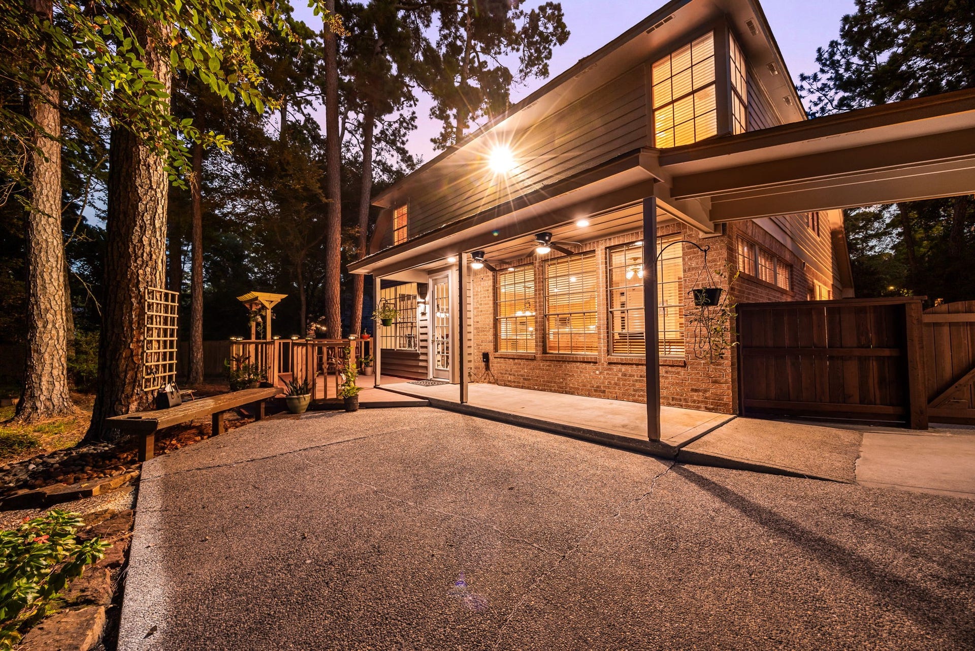 205 Purple Slate Place, The Woodlands, TX 77381 The expansive back exterior serves as an exceptional retreat, showcasing a large covered patio area illuminated by recessed lighting and equipped with outdoor ceiling fans. Nestled against a scenic backdrop of towering pines, this outdoor living space features a mix of a concrete patio slab and a raised wood deck walkway.