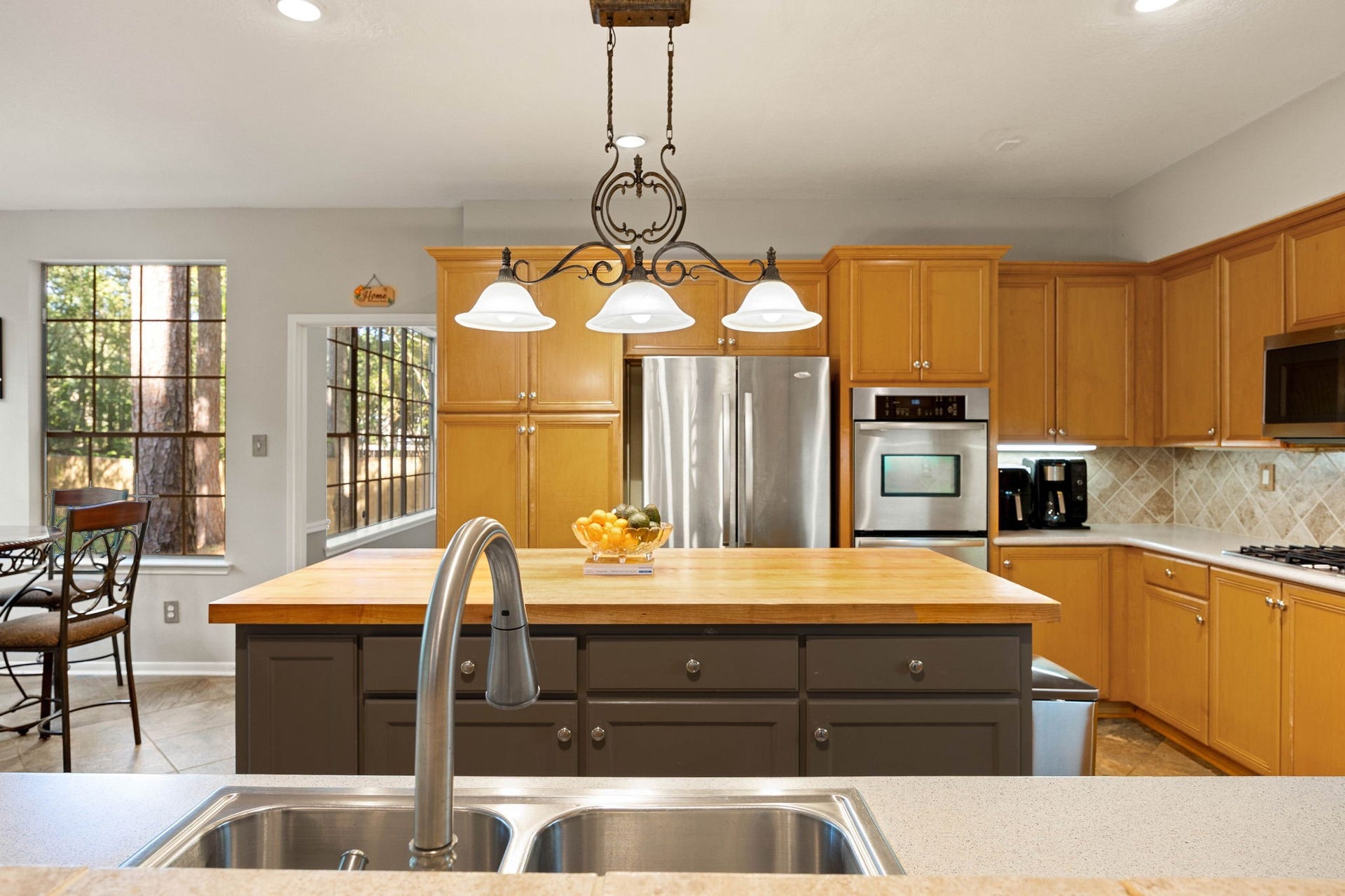205 Purple Slate Place, The Woodlands, TX 77381 The central half-bar layout provides the ultimate setup to prep meals while staying fully connected with guests hanging out in the living spaces. This viewpoint highlights the vast counter space, abundant cabinet storage, and premium built-in appliances that define the kitchen's perimeter. Large surrounding windows offer continuous glimpses of the wooded exterior, filling the entire culinary zone with a bright and airy energy.
