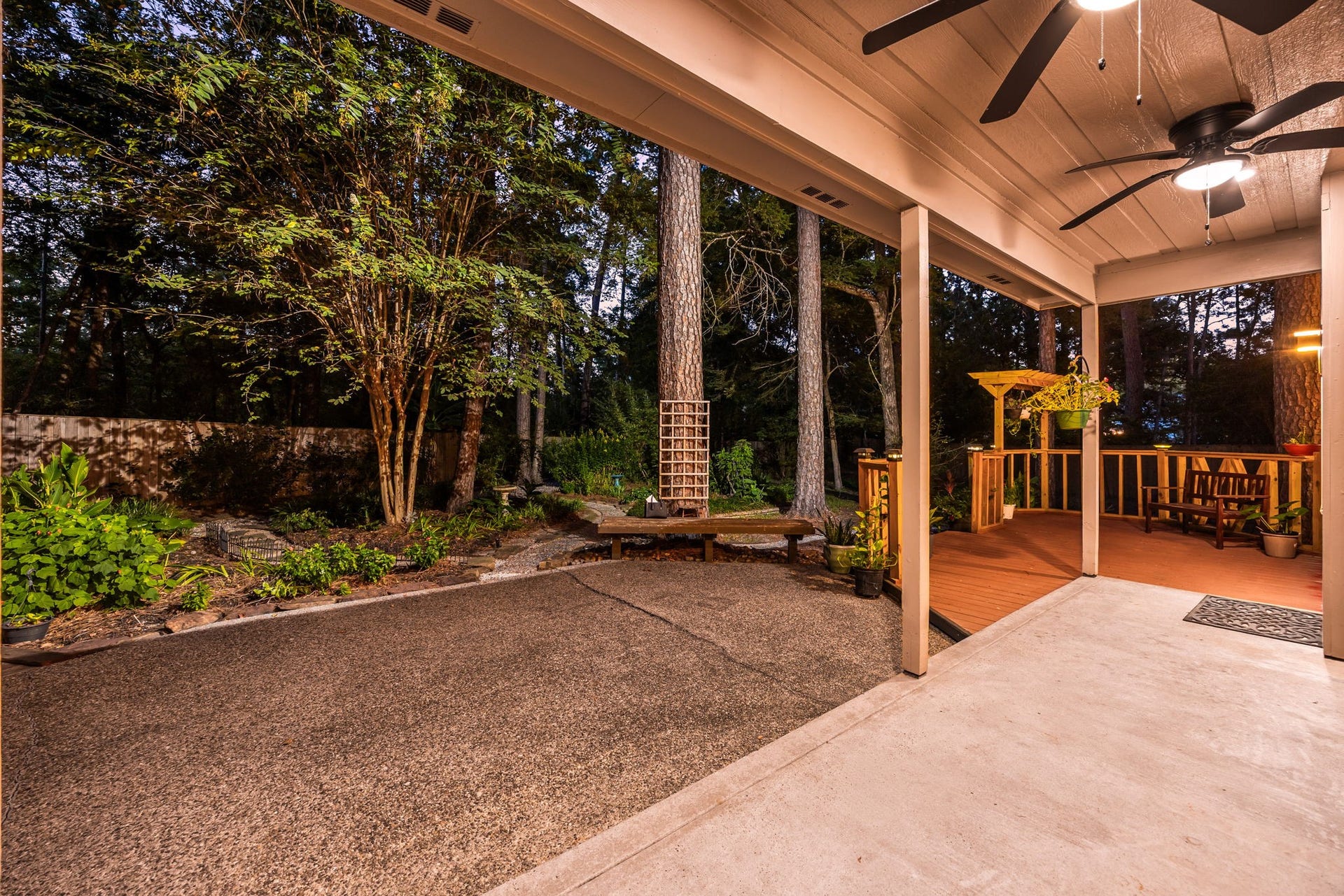 205 Purple Slate Place, The Woodlands, TX 77381 This peaceful vantage point illustrates the beautiful blend of covered shelter and open-air space that defines the home's rear exterior. The deep patio awning allows for year-round outdoor enjoyment, flowing effortlessly out onto the private grounds. Enveloped by towering pines and lush greenery, the split-level concrete and decking layout creates distinct areas for hosting summer gatherings or simply relaxing in complete, natural seclusion.