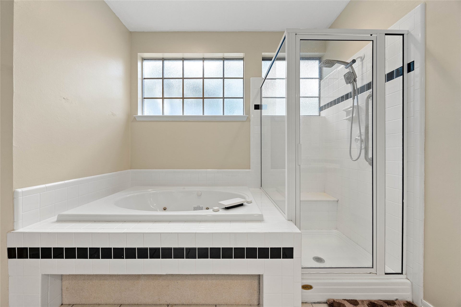 205 Purple Slate Place, The Woodlands, TX 77381 This close-up perspective showcases the convenient layout of the bathroom's dedicated soaking and shower zones. The oversized whirlpool tub offers an ideal spot to unwind, while the adjacent shower enclosure maximizes space with its built-in seating ledge and corner shelving. Crisp neutral walls and classic white masonry accents tie the distinct areas together, emphasizing a clean and timeless design.