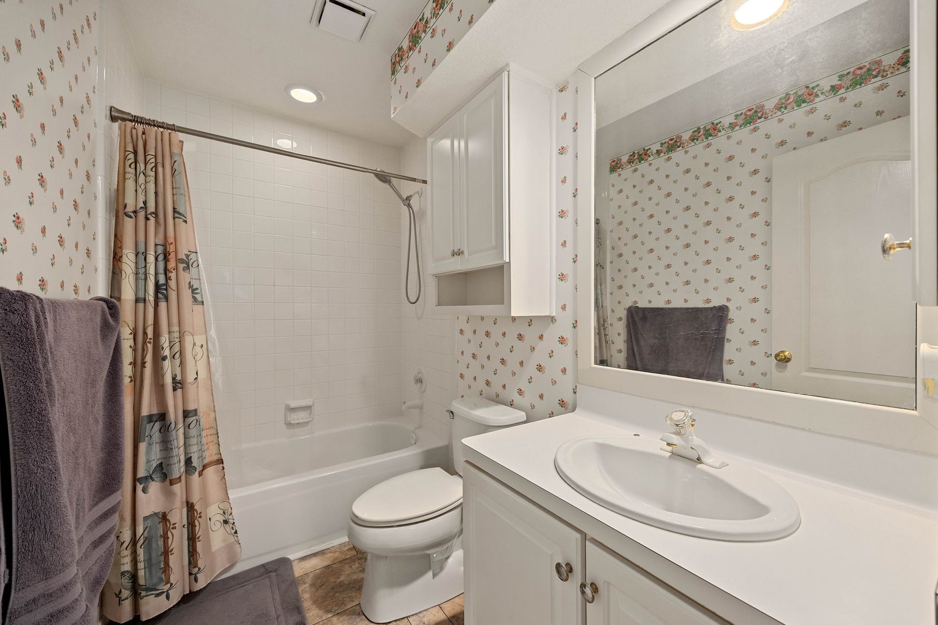 205 Purple Slate Place, The Woodlands, TX 77381 An attached secondary bathroom layout offers privacy and effortless functionality. The space features a clean white vanity station, an overhead storage cabinet, and a standard tub/shower enclosure. Bright lighting and neutral porcelain elements combine to create a highly practical setup that meets all daily routine needs.