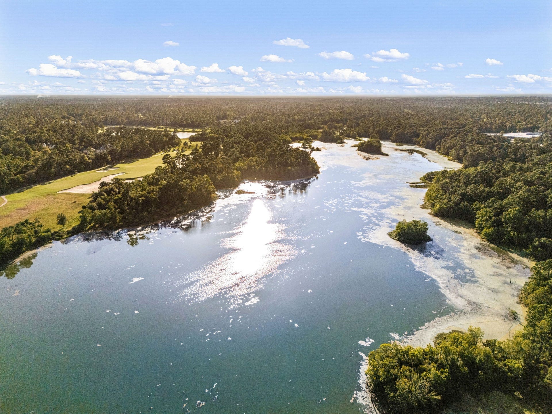 205 Purple Slate Place, The Woodlands, TX 77381 This spectacular bird's-eye view highlights the breathtaking natural beauty surrounding the community, showcasing the expansive, sunlit lake bordering the prestigious Palmer Golf Course.