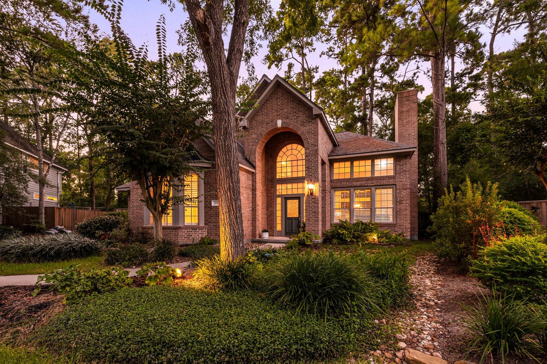 205 Purple Slate Place, The Woodlands, TX 77381 Welcome to 205 Purple Slate, a stunning brick estate nestled in a serene, wooded setting in the heart of The Woodlands. From the moment you arrive, you are greeted by mature towering pines, professional uplighting, and a grand arched entryway that radiates curb appeal. Large architectural windows showcase a truly magnificent home that beautifully blends timeless elegance with its lush natural surroundings.