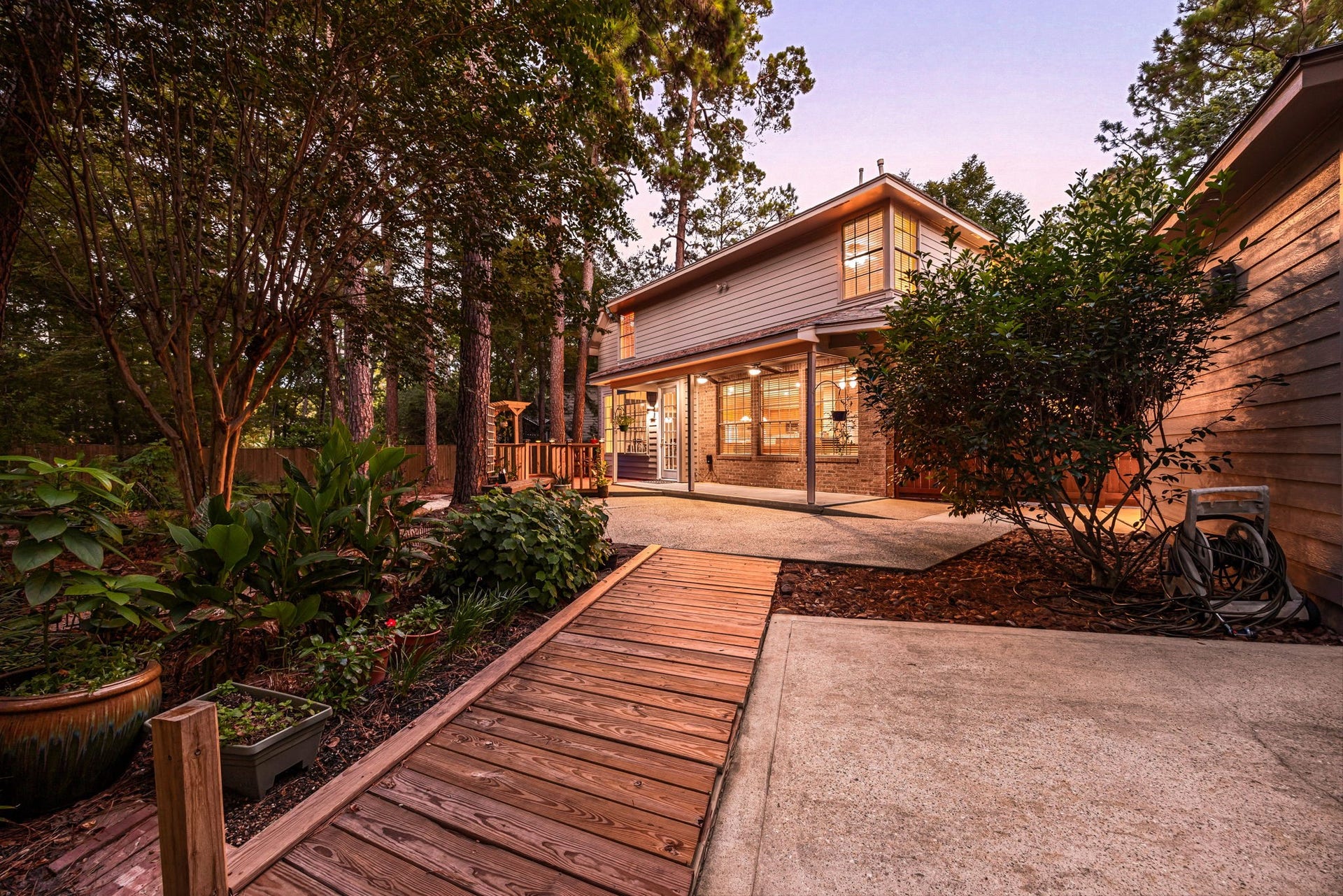 205 Purple Slate Place, The Woodlands, TX 77381 A custom wooden boardwalk trail meanders through the lushly landscaped yard, seamlessly connecting the separate outdoor living zones. This rustic timber pathway links the covered patio and raised deck area, guiding you through a park-like landscape.