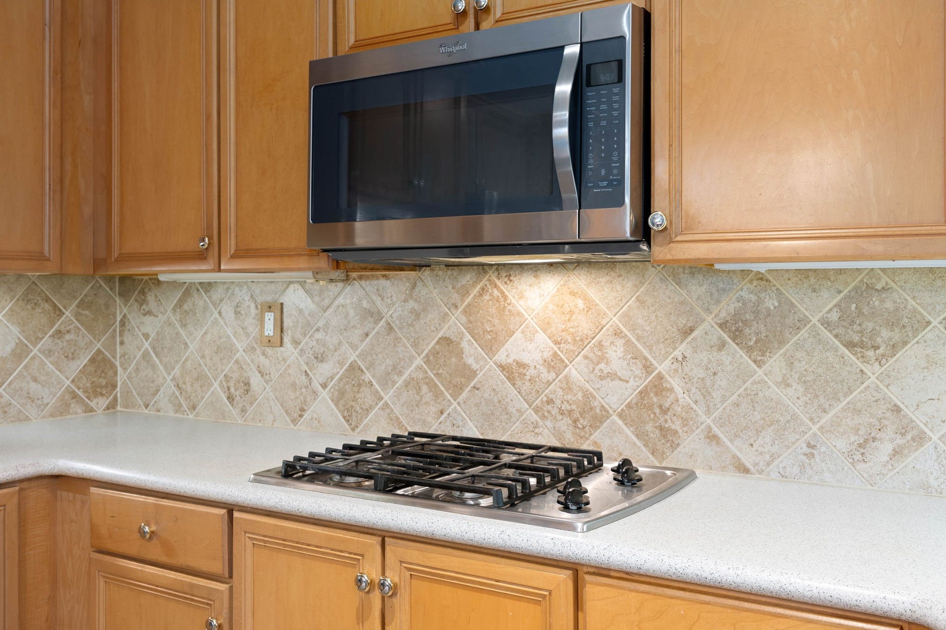 205 Purple Slate Place, The Woodlands, TX 77381 The kitchen's functional elegance is highlighted by this premium gas cooktop and integrated stainless steel microwave setup. Rich natural wood cabinets offer extensive storage options right at your fingertips, while the neutral stone tile backsplash adds a sophisticated texture to the space. Bright under-cabinet lighting illuminates the expansive counter surface, creating a highly practical and inviting workspace.