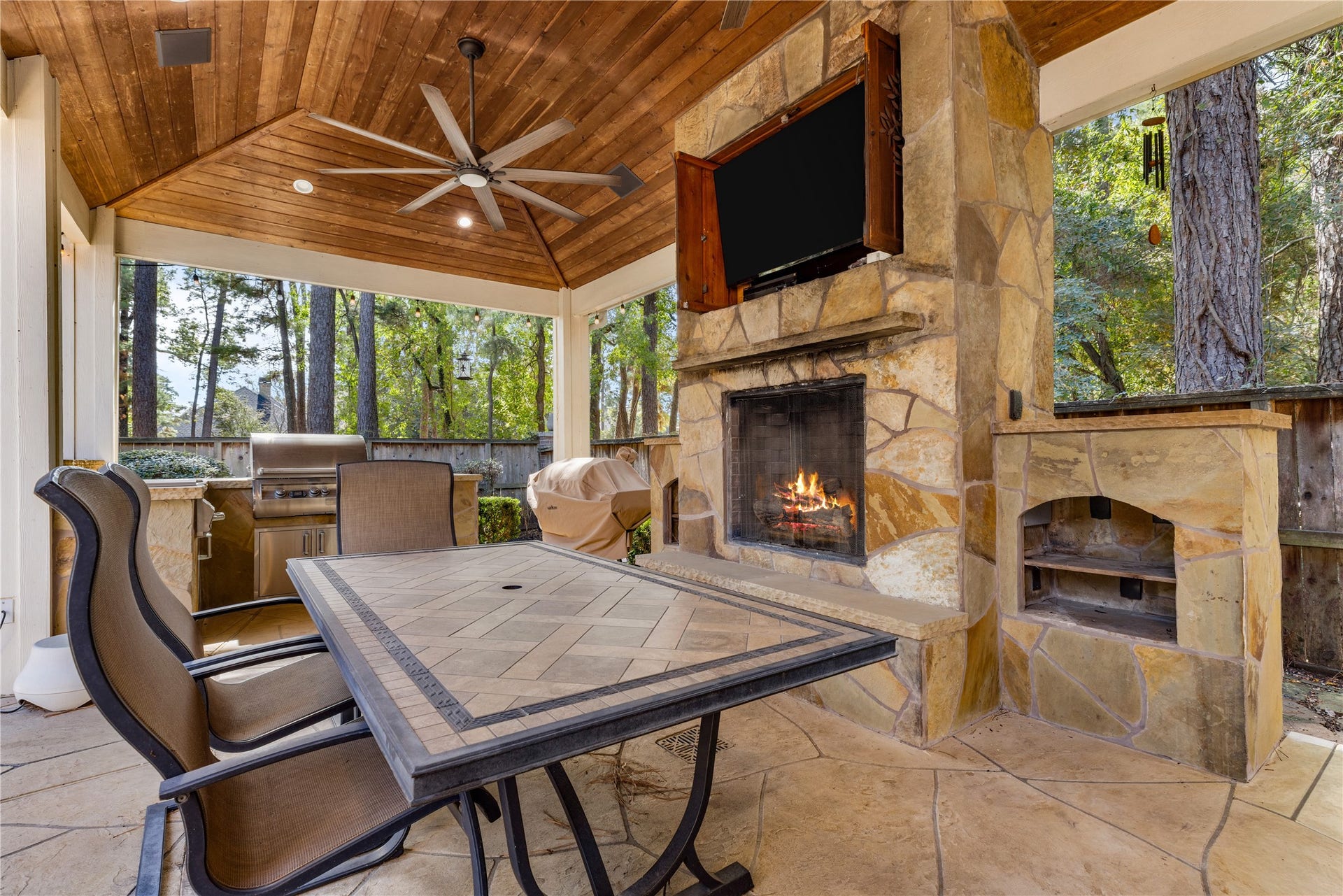 2214 Kings Trail, Kingwood, TX 77339 Outdoor living area with TV included and outdoor speakers. Fireplace fire has been digitally added for illustrative purposes.
