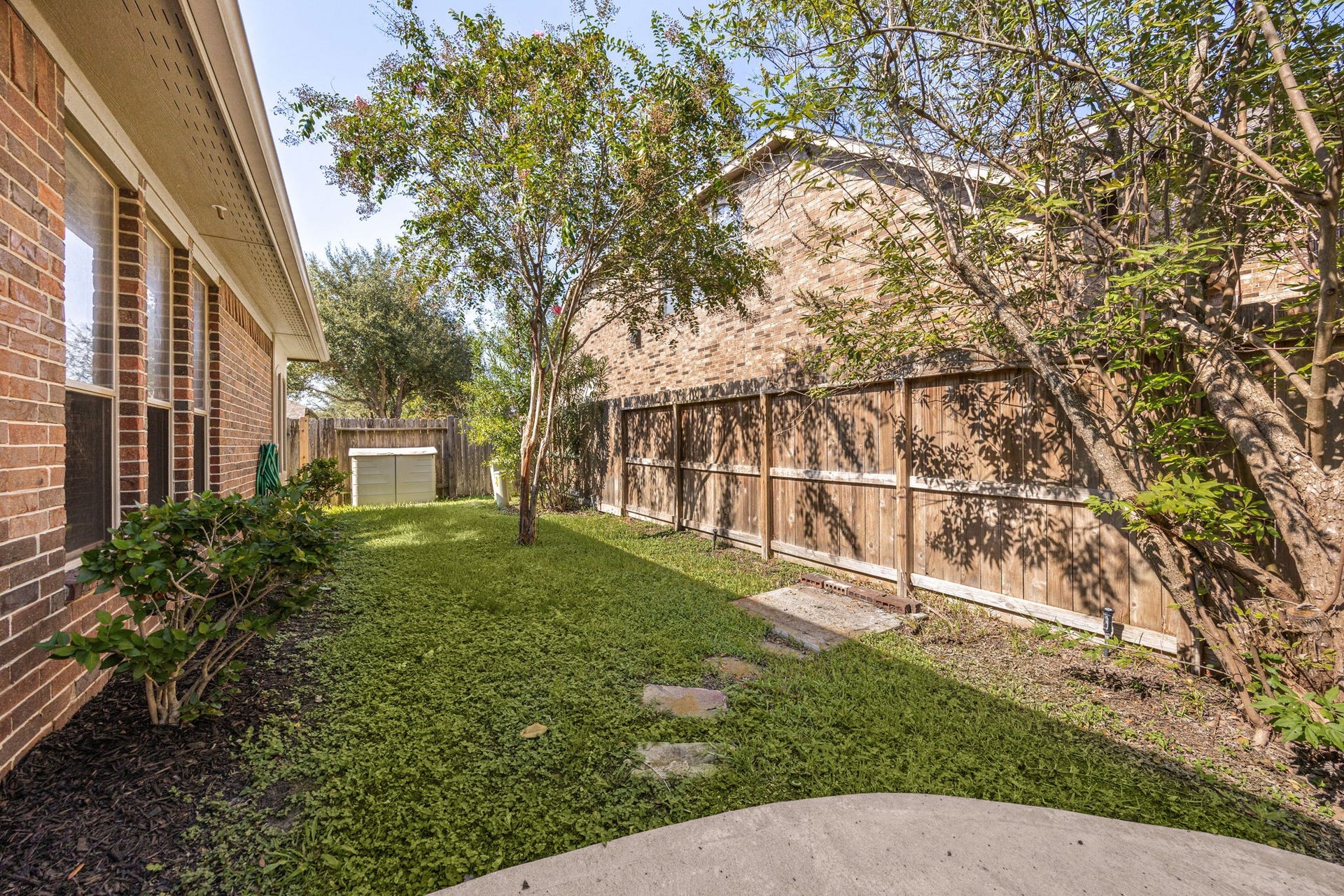 9430 Amethyst Arbor Lane, Katy, TX 77494 This side view of the backyard highlights a beautifully shaded green space and a secure wooden privacy fence.