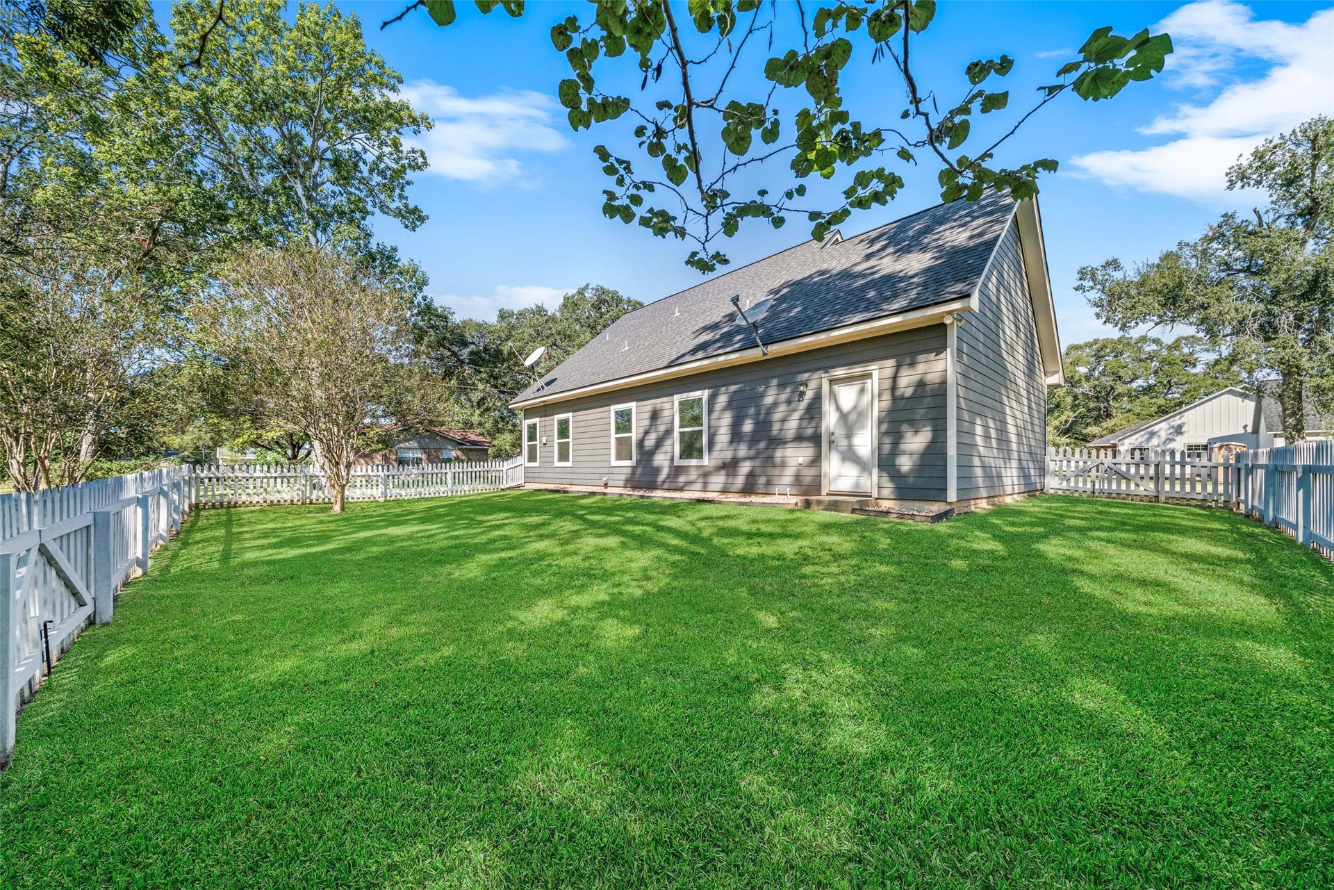 1125 Galveston Street, Hempstead, TX 77445 Additional backyard view highlighting the homes stone exterior, fenced lawn, and mature trees.