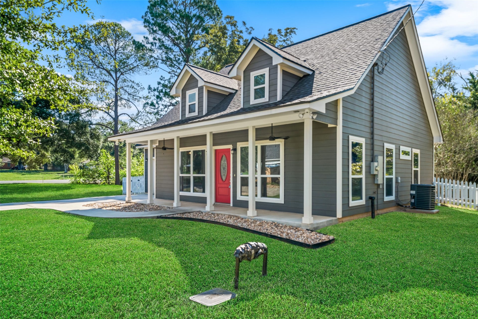 1125 Galveston Street, Hempstead, TX 77445 Angled front view highlighting the covered porch, red entry door, dormer windows, and mature shade trees.