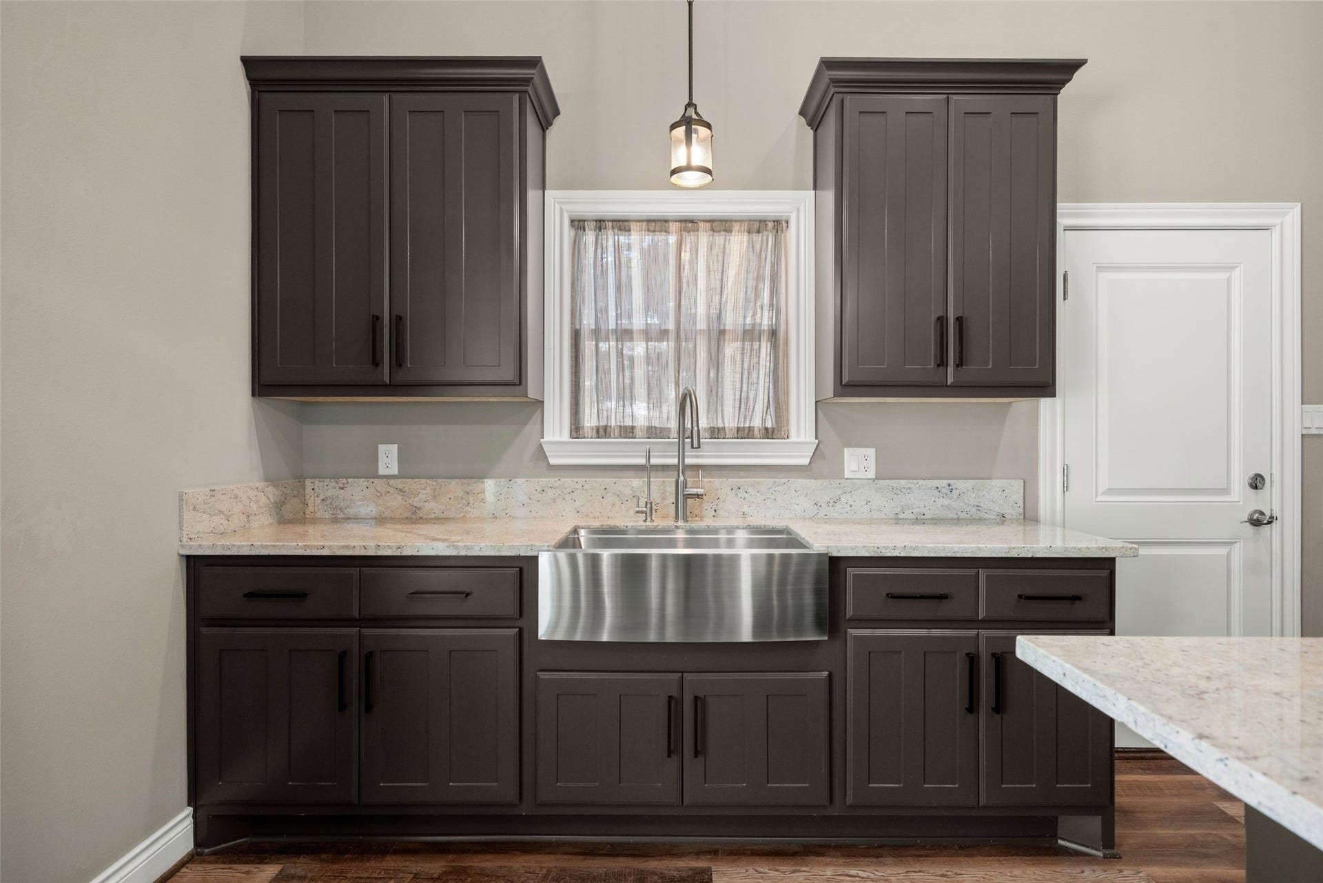 1125 Galveston Street, Hempstead, TX 77445 Kitchen detail featuring dark cabinetry, light countertops, a stainless steel apron-front sink, and pendant lighting.