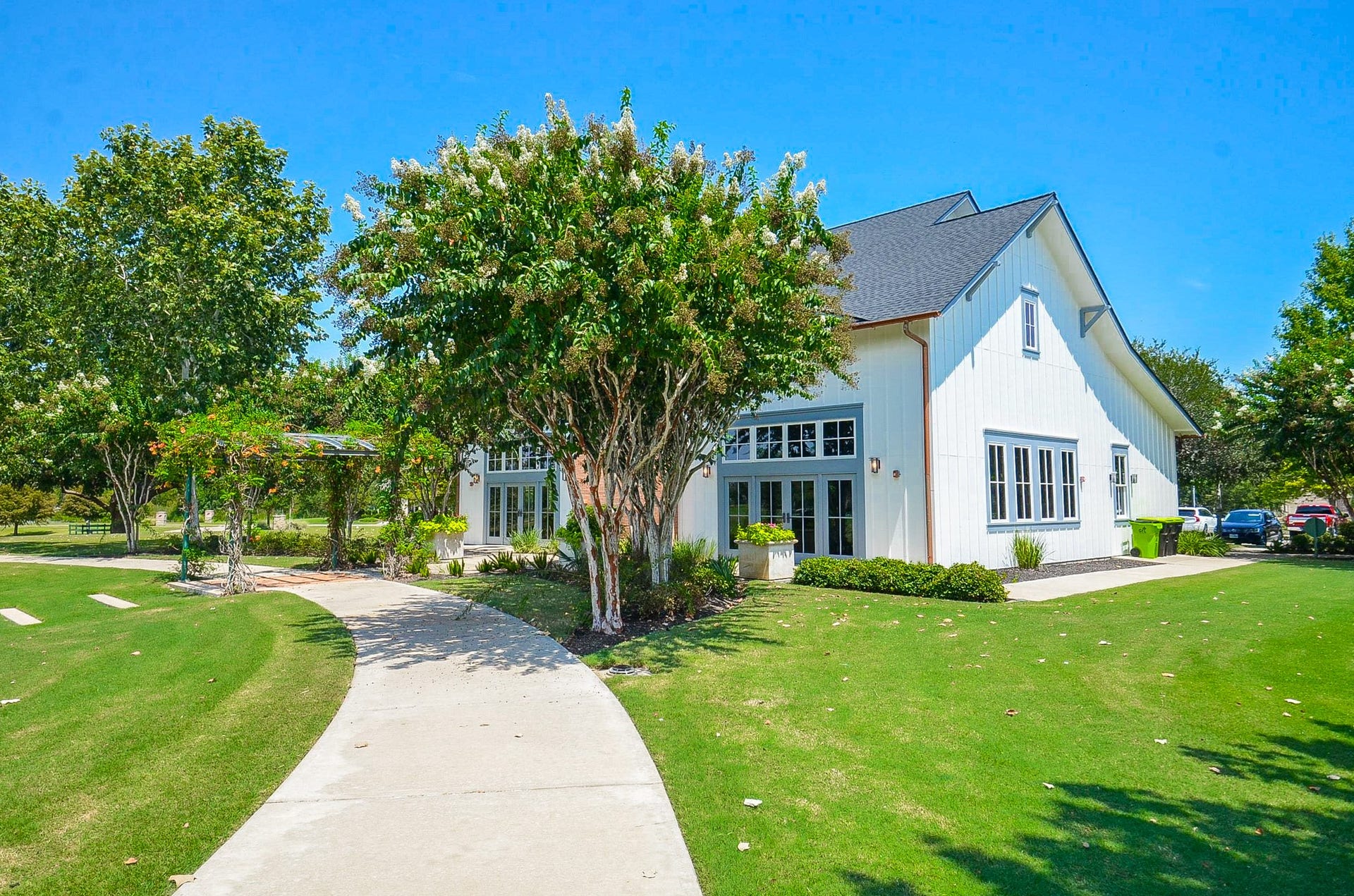 30706 Hawthorn Glen Court, Fulshear, TX 77441 Charming modern farmhouse with crisp white siding and a beautifully manicured lawn, surrounded by lush trees and a welcoming pathway.