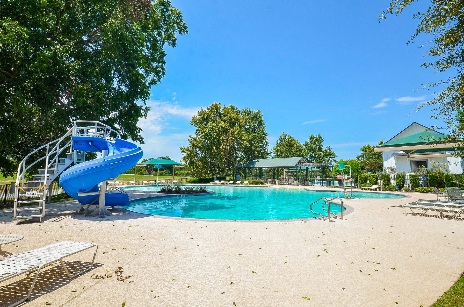 30706 Hawthorn Glen Court, Fulshear, TX 77441 Enjoy outdoor leisure with a spacious pool featuring a fun water slide, surrounded by lush greenery and ample seating.